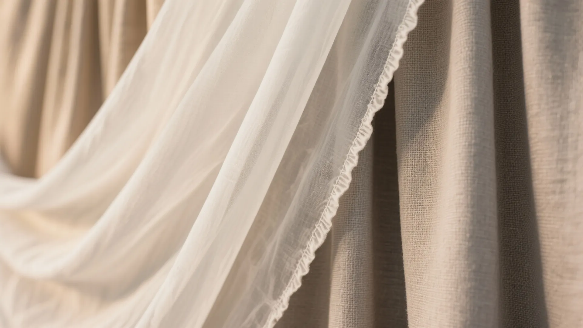 White sheer curtain hanging over thick beige fabric material with soft woven texture and sunlight