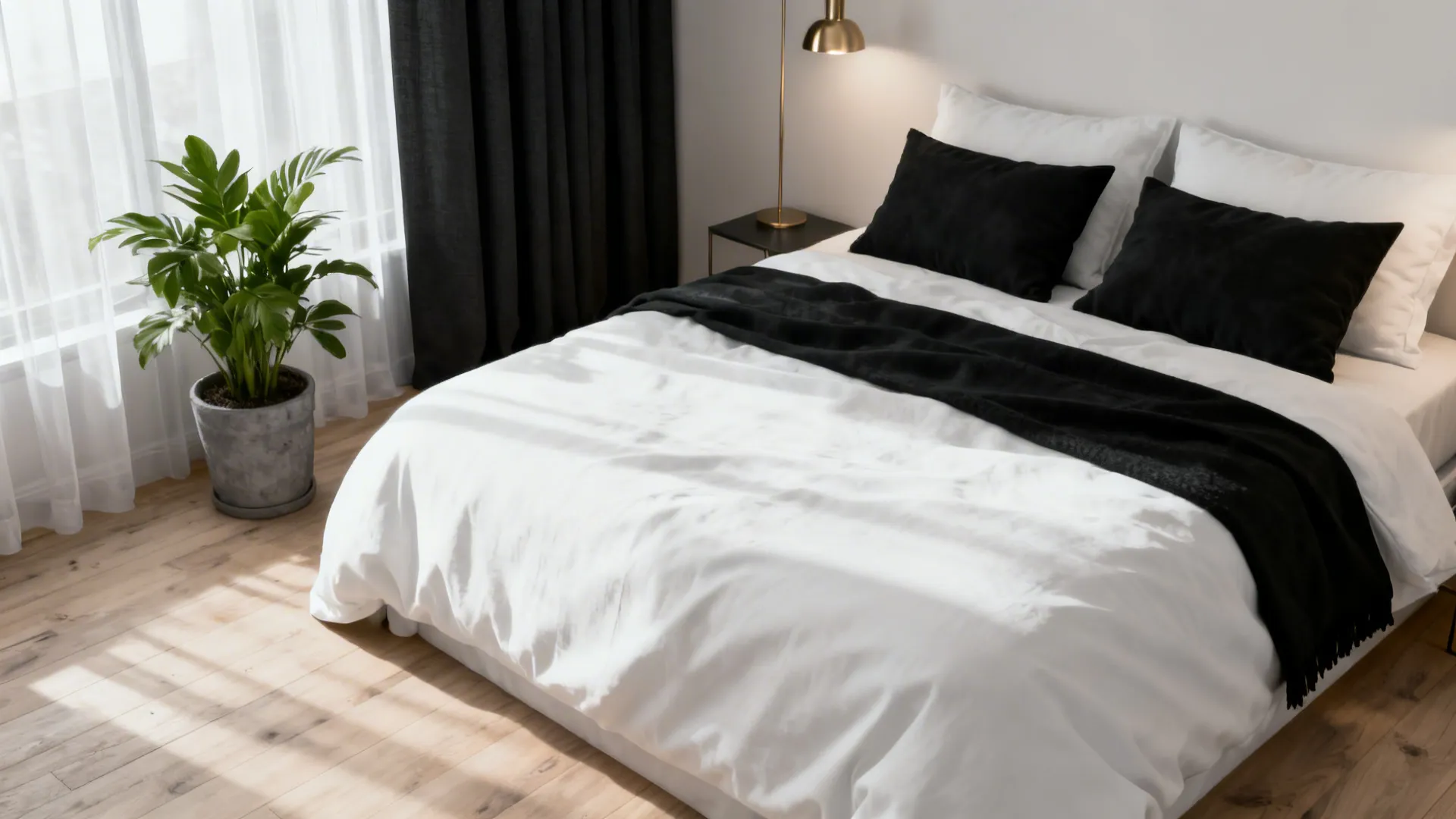 Cozy black-and-white bedroom vignette with white bedding, black accents, warm wood floor and a green plant.