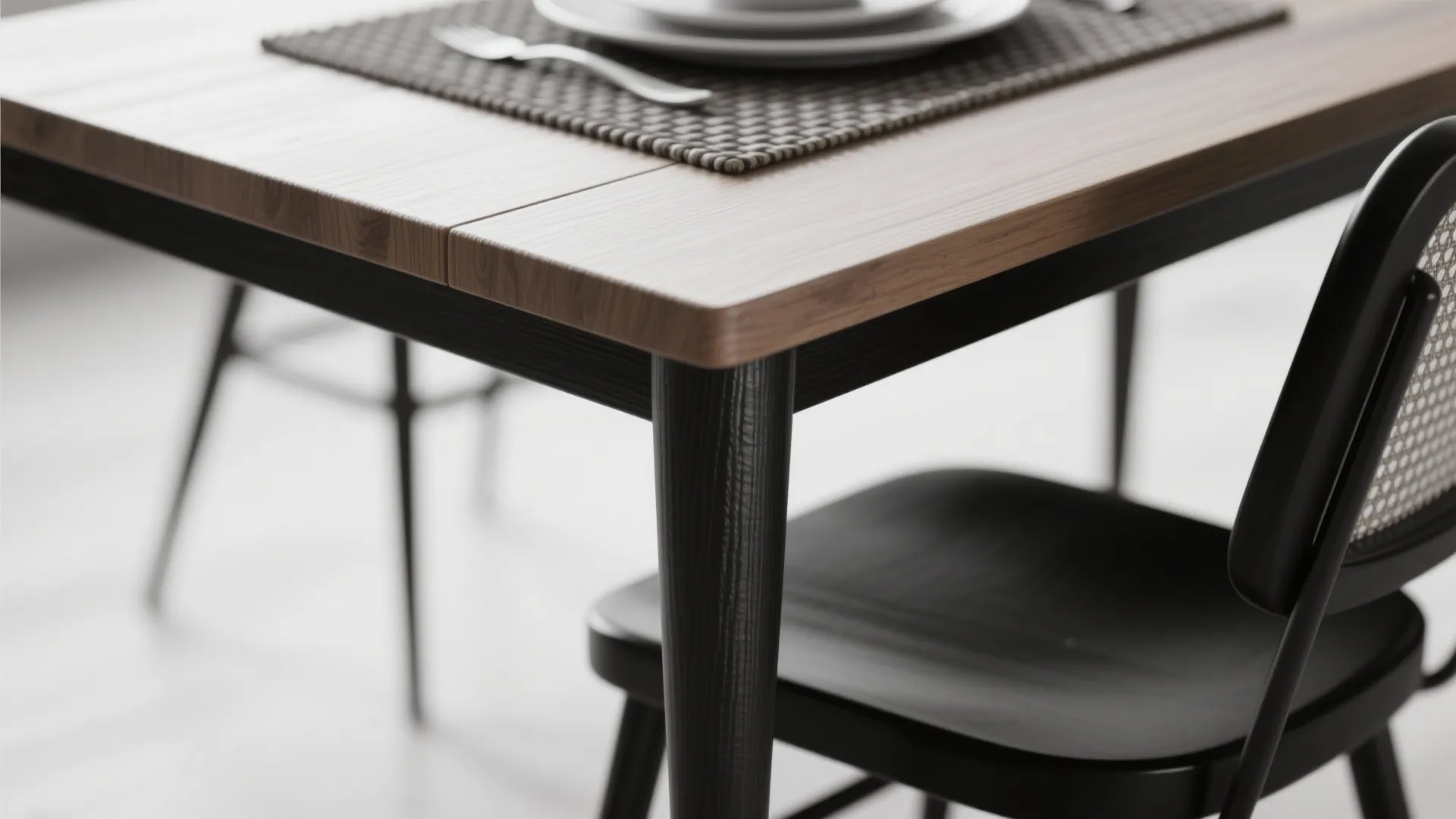 Close-up of wooden table edge, woven placemat and black-and-white chair leg showing texture