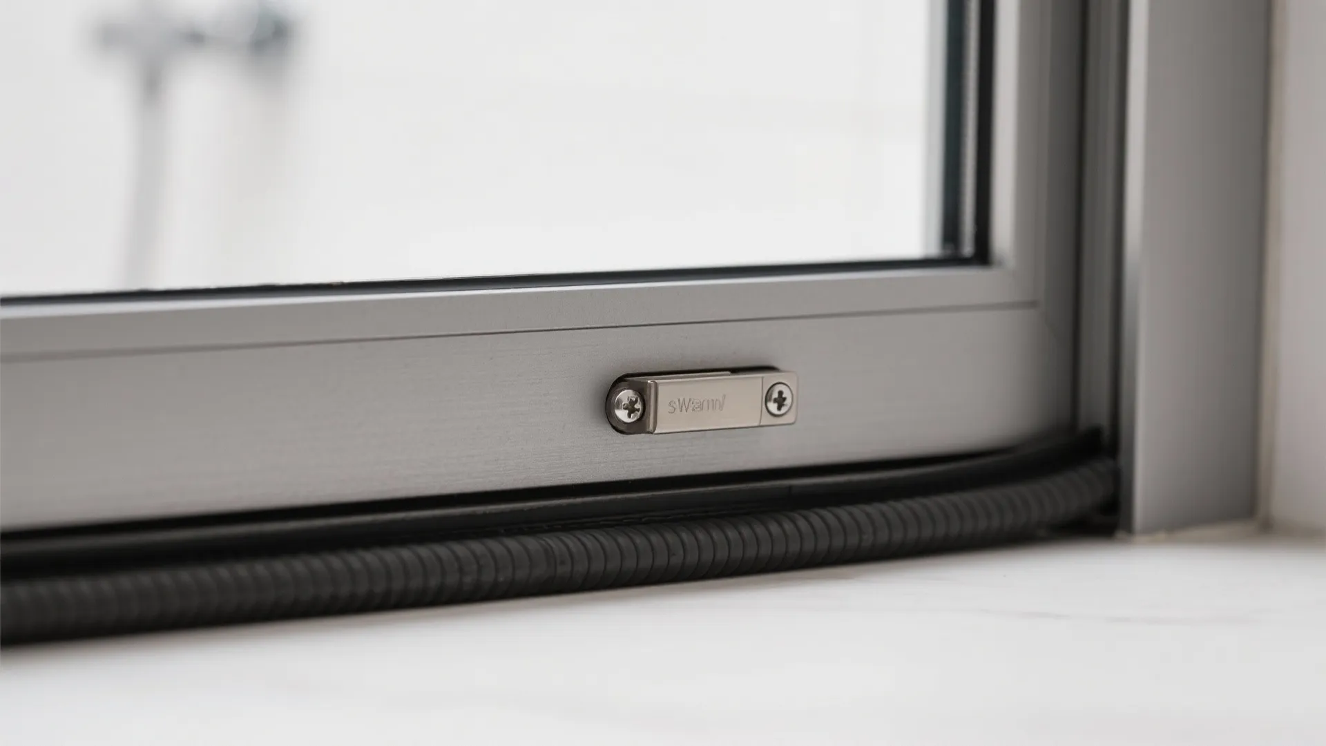 Close up of silver metal window frame featuring small locking mechanism and black weather stripping