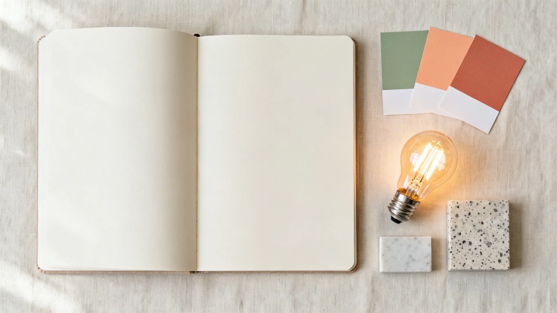 Flat lay with color chips, quartz and terrazzo samples, and a warm LED bulb beside a notebook.