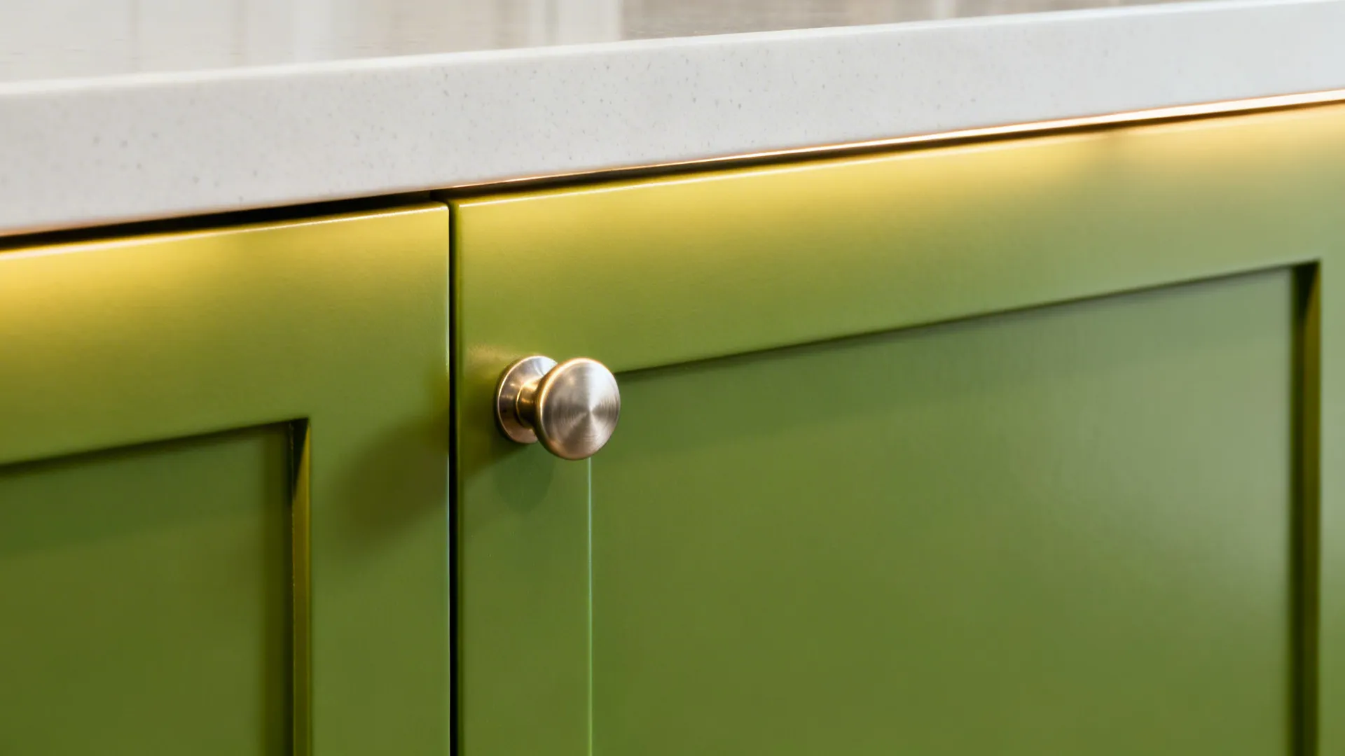 Macro of apple-green cabinet with brushed nickel pull beside a light quartz counter under warm light.