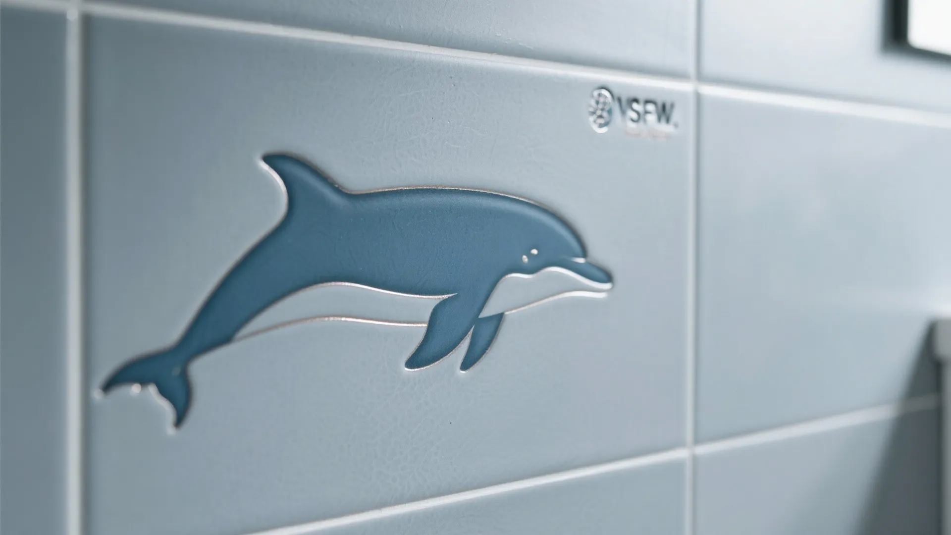 Close up of light blue wall tiles featuring a decorative blue dolphin pattern design element