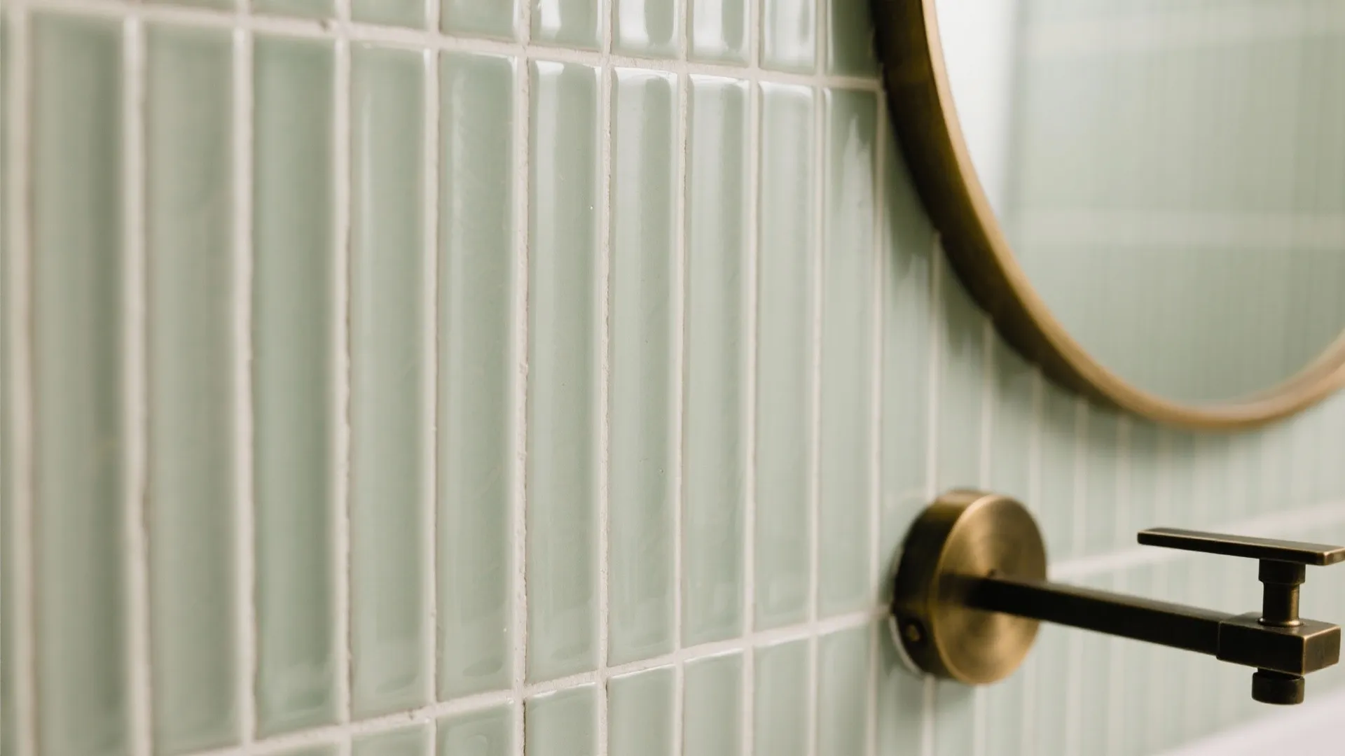 Close up view of light green narrow wall tiles with round mirror and metal fixture