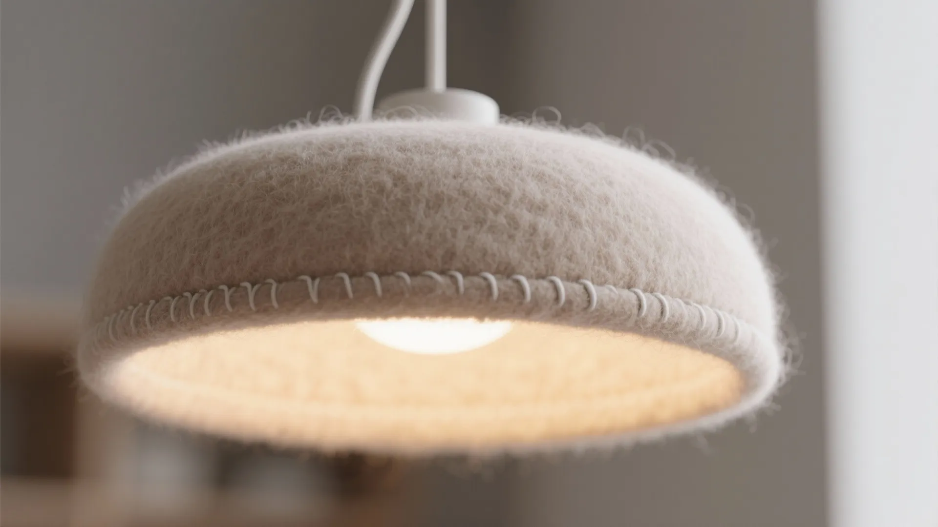 Close up view of a round white felt hanging light fixture with visible stitching details