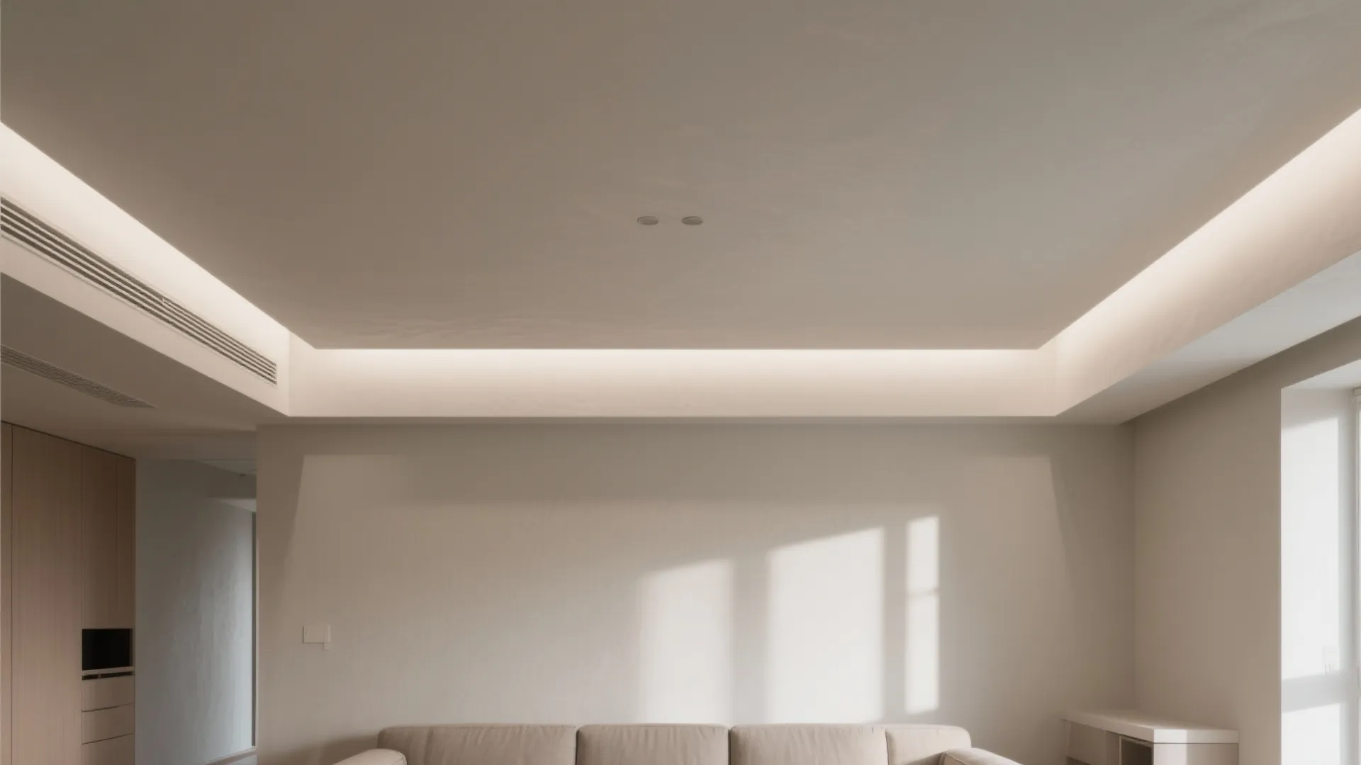 Minimalist living room with white walls and hidden ceiling light strip above a beige sofa