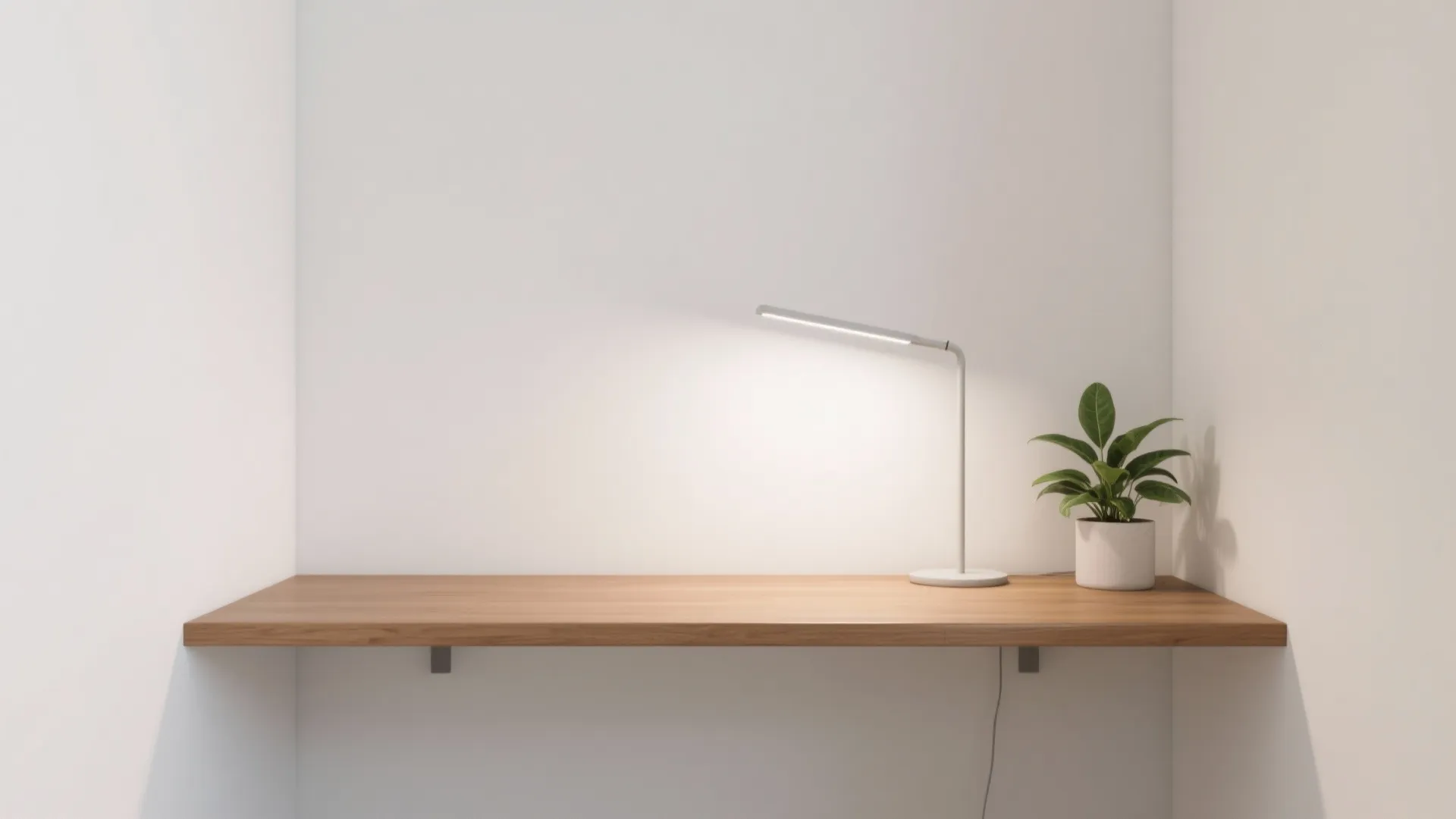 Minimalist wooden floating desk mounted on white wall with white table lamp and small plant