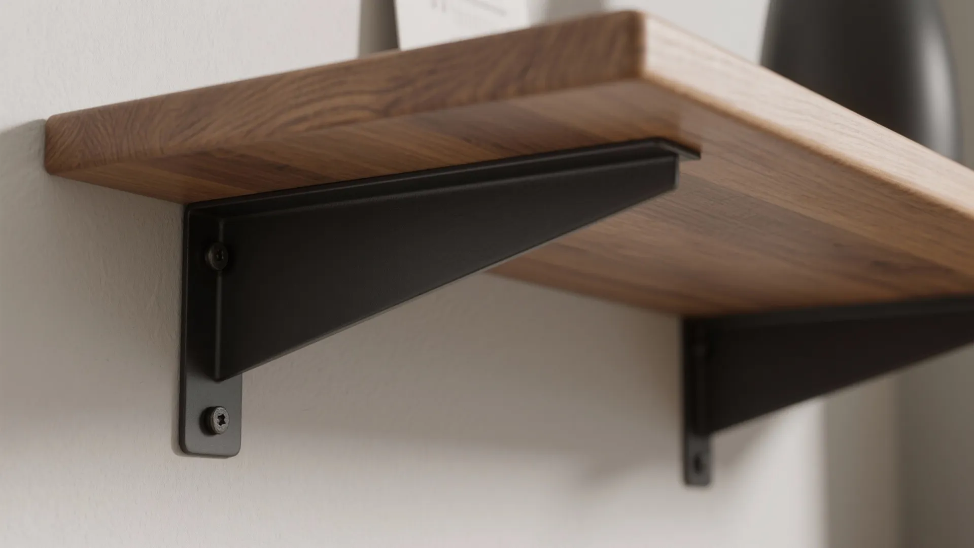 Close up of a wooden wall shelf supported by black metal brackets on white wall