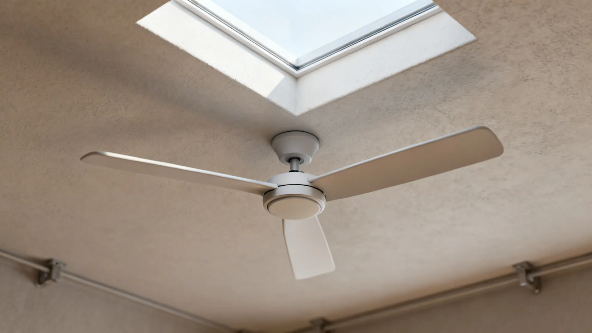 Close-up of a slim ceiling fan mounted under a skylight showing precise alignment and neutral plaster ceiling.