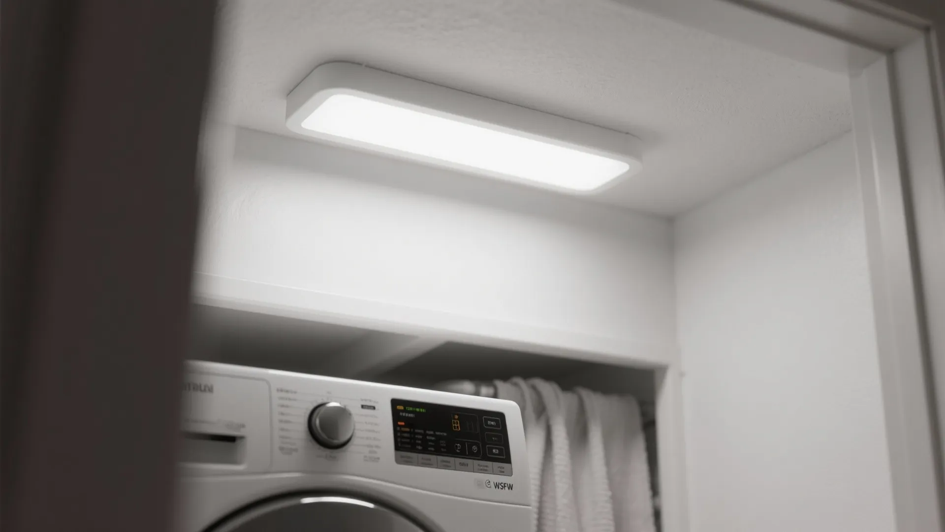 Modern rectangular ceiling light illuminating a laundry area above a white washing machine and towels