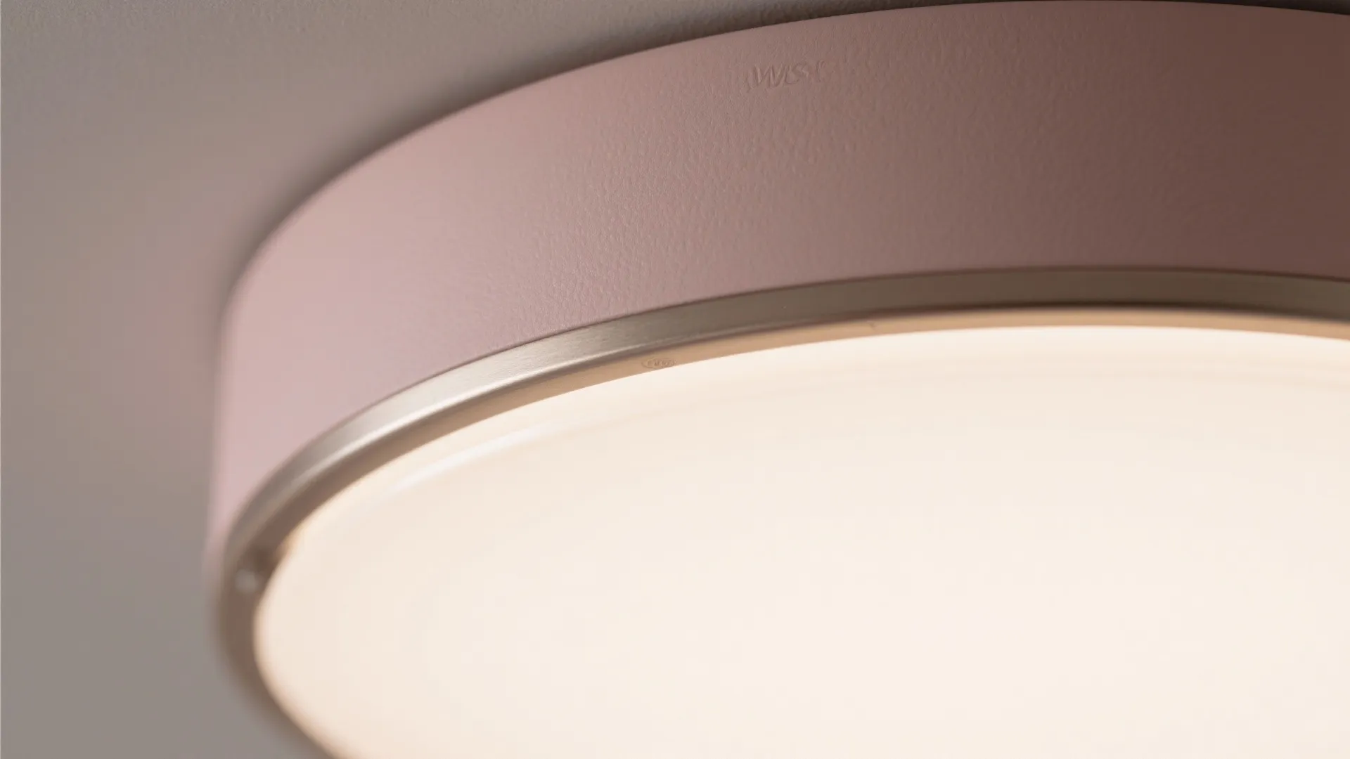 Close up view of a round pink ceiling light fixture with a gold rim and smooth