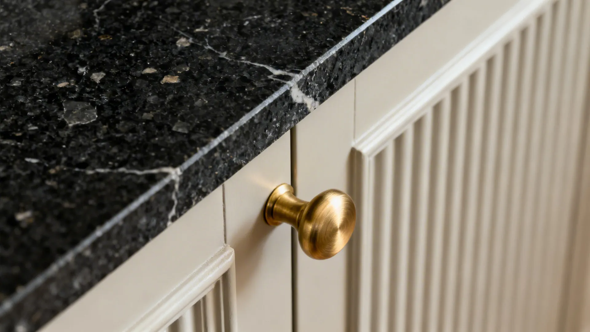 Close-up of black granite edge, fluted cabinet texture, and satin brass pull.