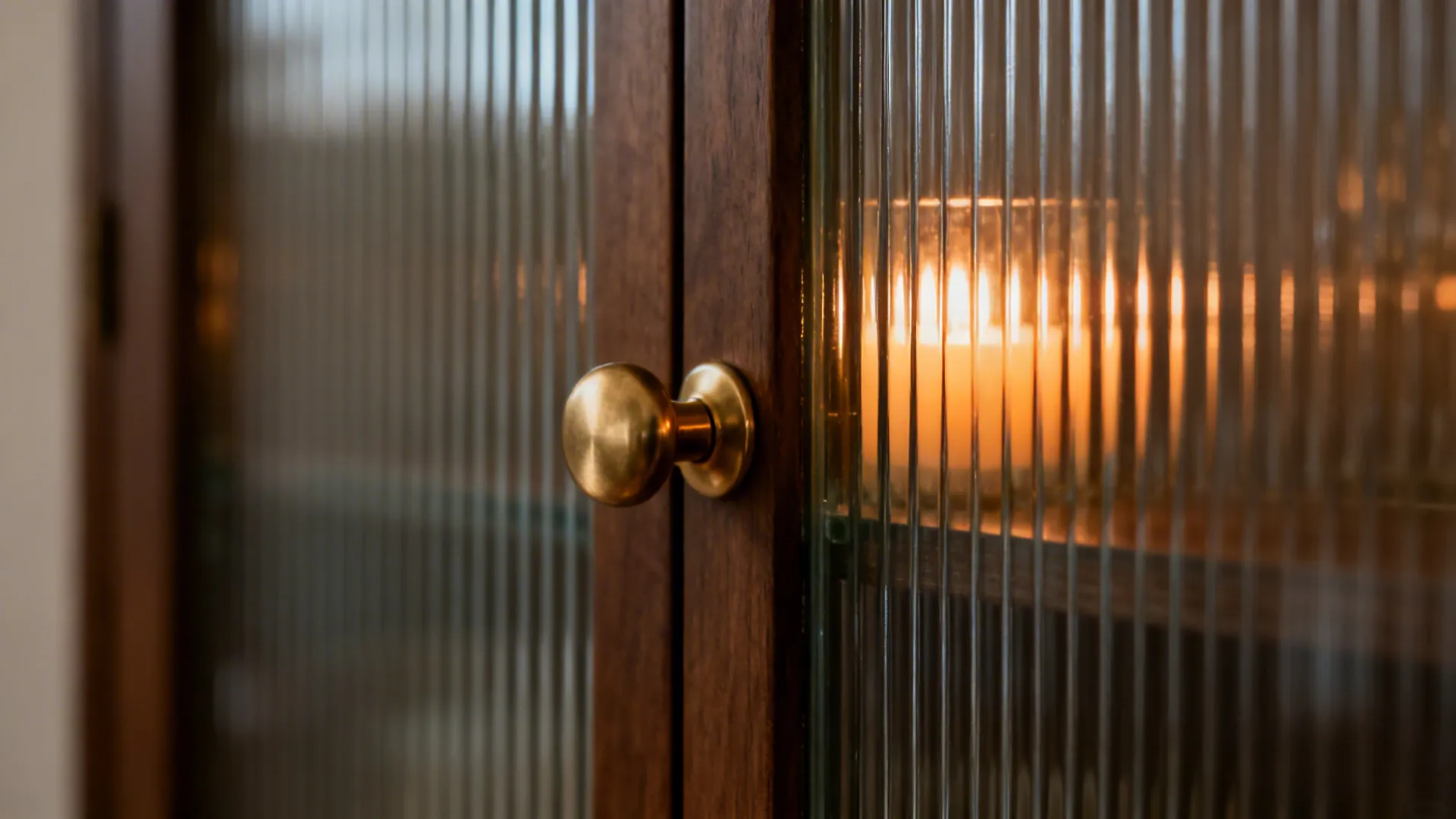 Macro of fluted glass with a satin brass pull shimmering in warm candlelight.