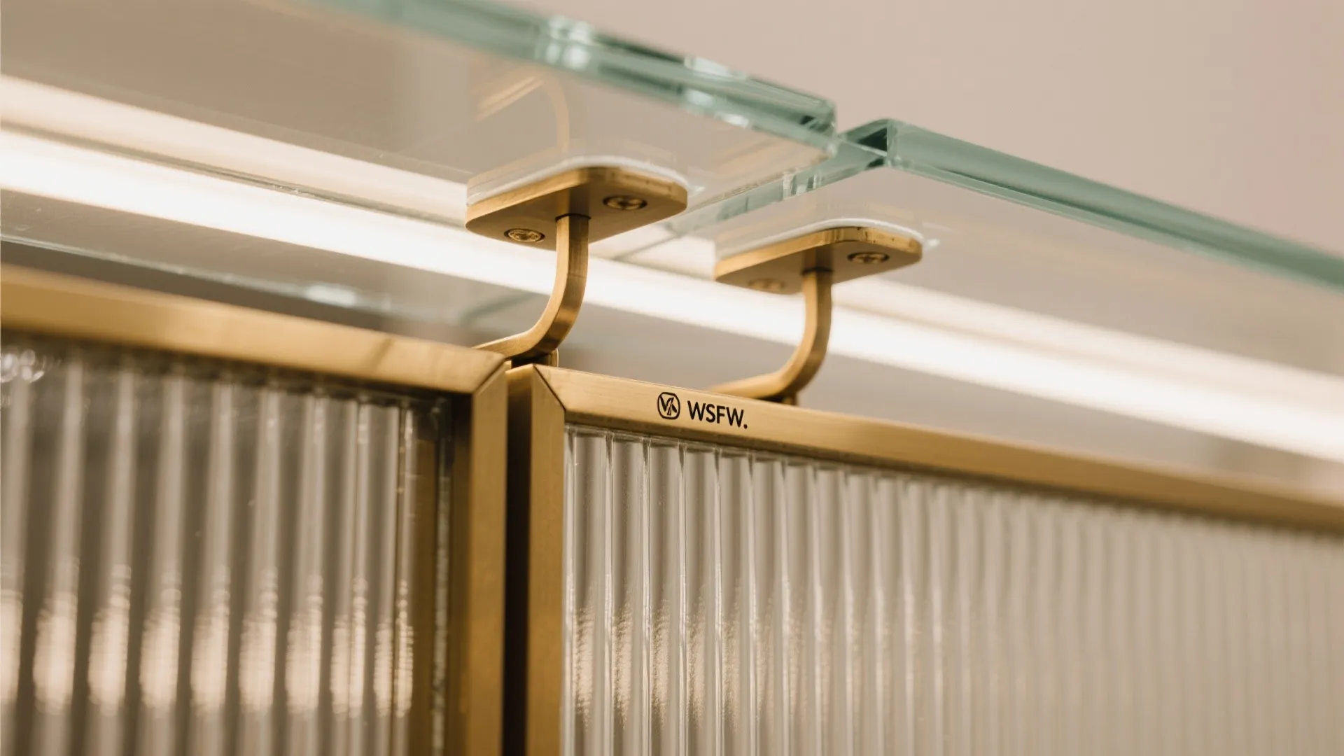 Close up of fluted glass cabinet doors with gold metal frames and glass shelf with lighting