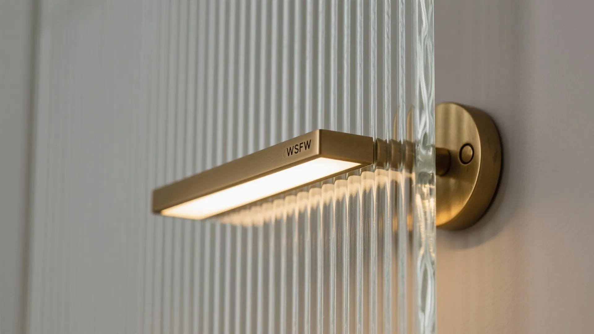 Close-up of fluted tempered glass with a slim brass handle and warm diffused lighting.