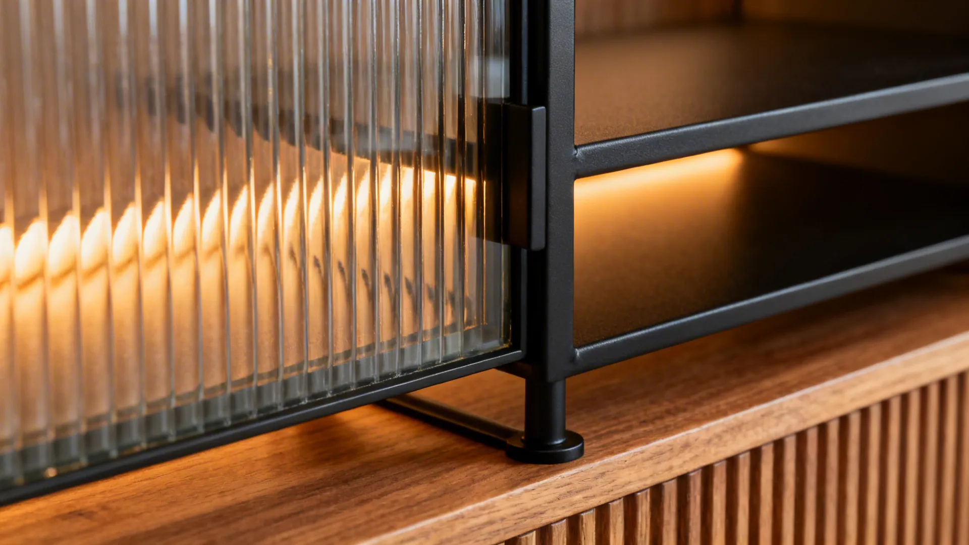 Macro of fluted glass cabinet glowing over a satin black metal shelf and ribbed oak detail.