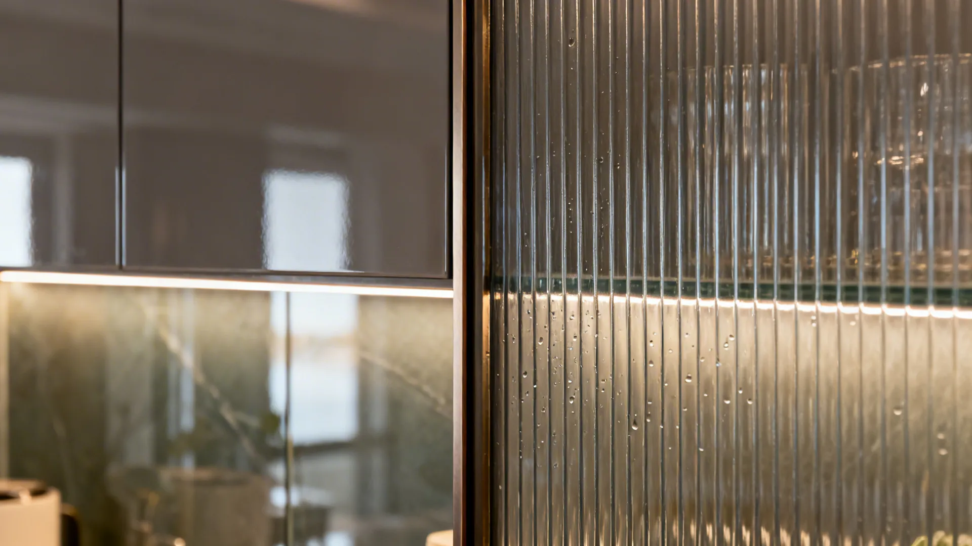 Macro detail of fluted glass cabinet door and glossy tempered glass backsplash with LED glow.