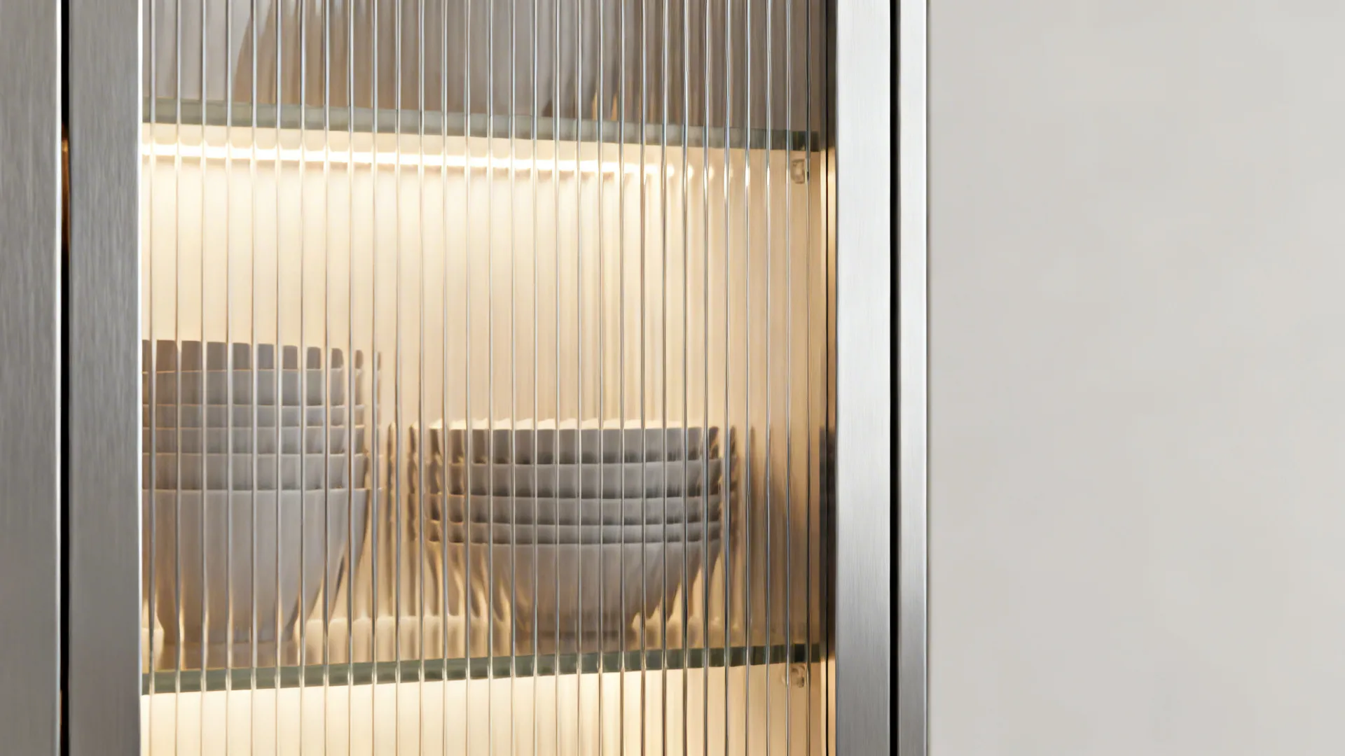 Close-up of fluted glass cabinet door with a slim metal frame and soft interior lighting.