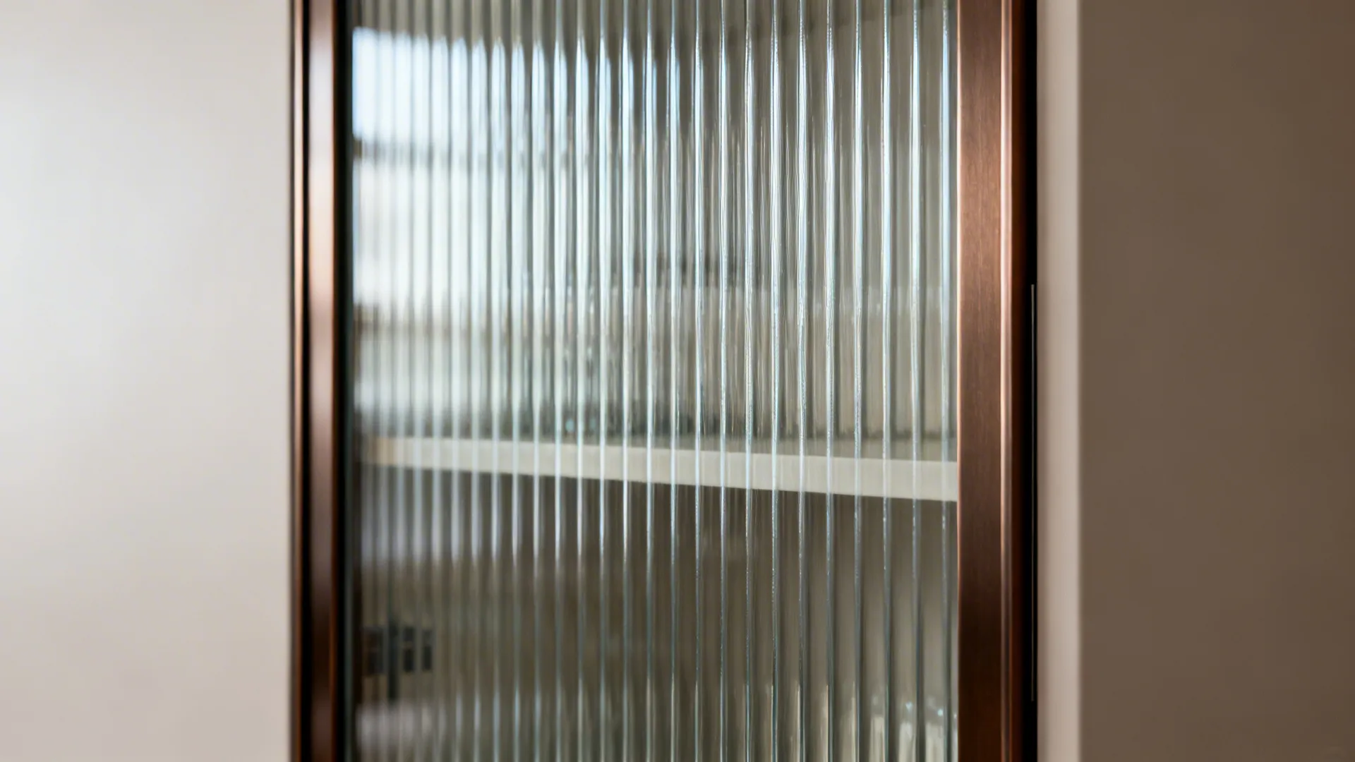 Close-up of fluted tempered glass in a slim bronze aluminum cabinet frame with soft lighting.