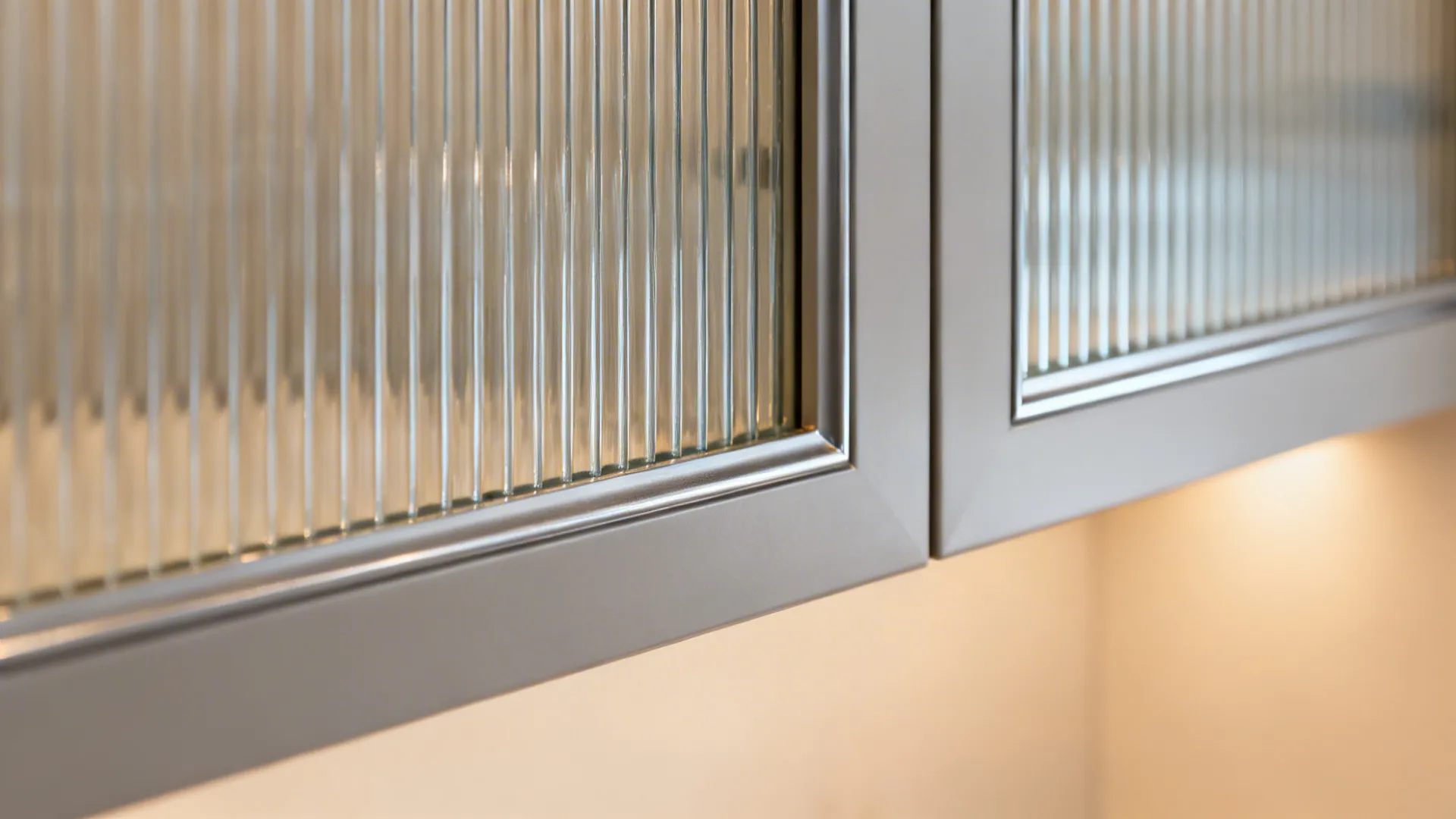 Close up of grey kitchen cabinet doors with textured glass panels and warm yellow lighting
