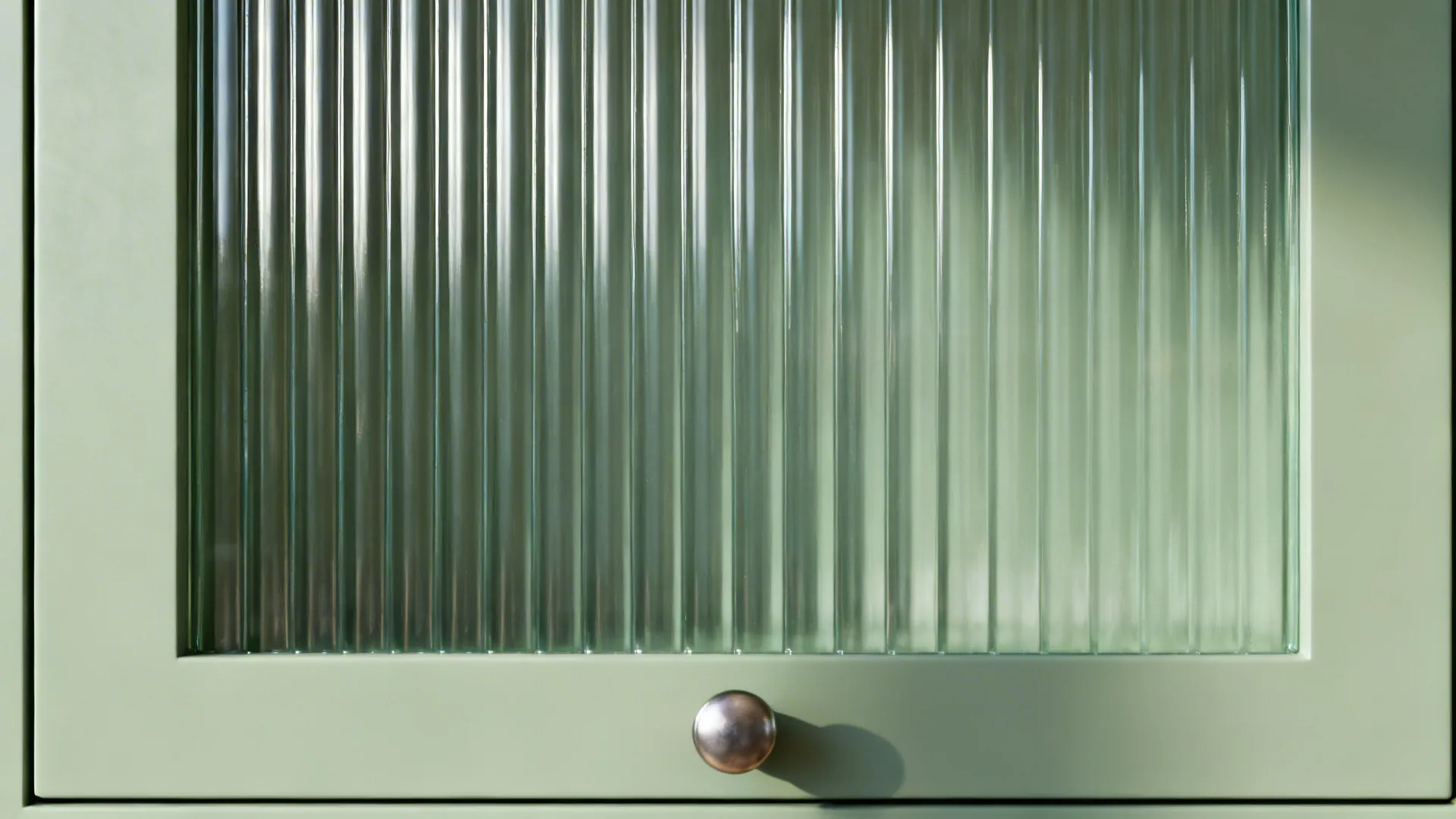 Macro view of sage-tinted reeded glass with vertical grooves and a minimal knob.