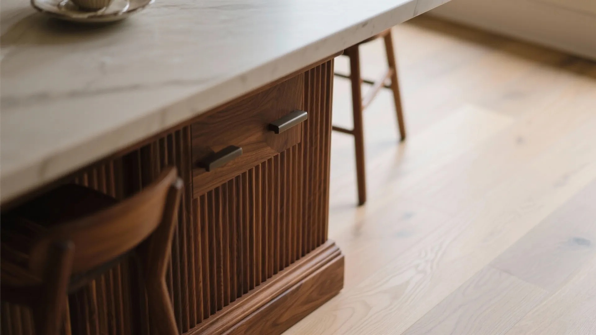 Macro of a fluted wood breakfast ledge and walnut toe-kick meeting light flooring.