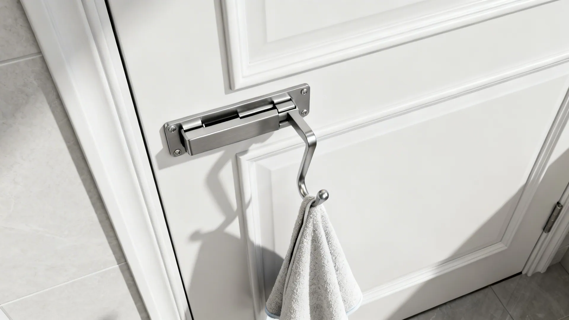 Silver metal hook installed on a white door hanging a grey towel in a bathroom