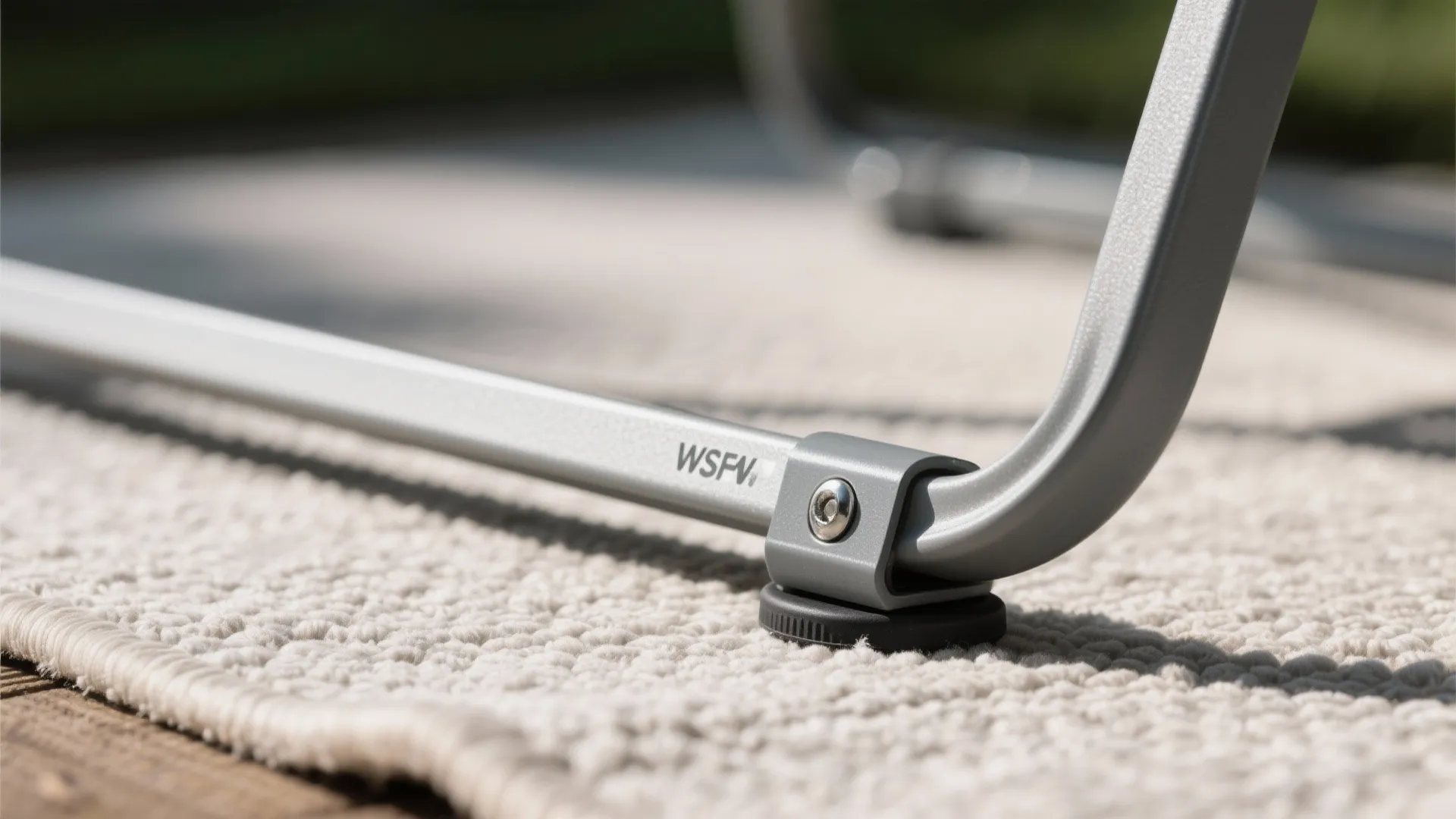 Close-up of a foldable chair’s hinge and rubber foot on a low-pile outdoor rug.