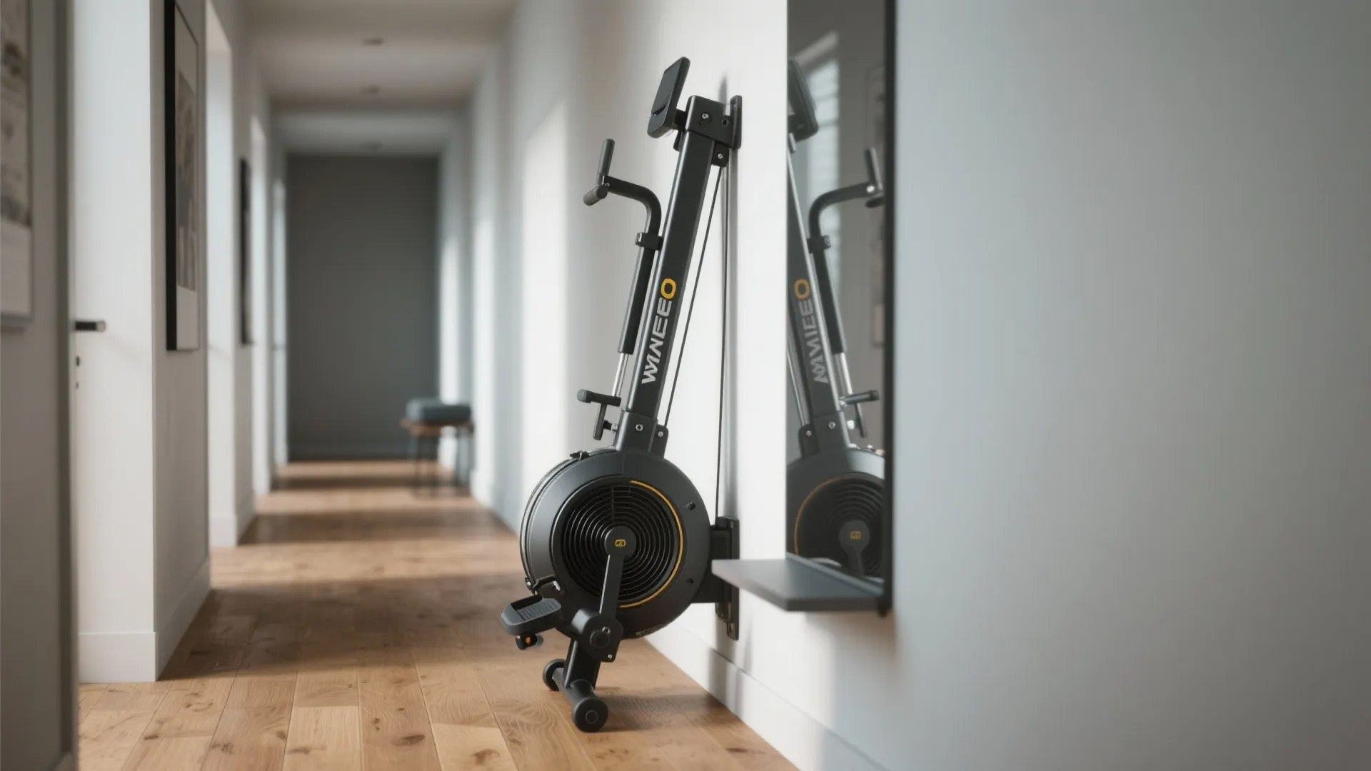 Black foldable rowing machine stored against a white wall in a hallway with wooden floor