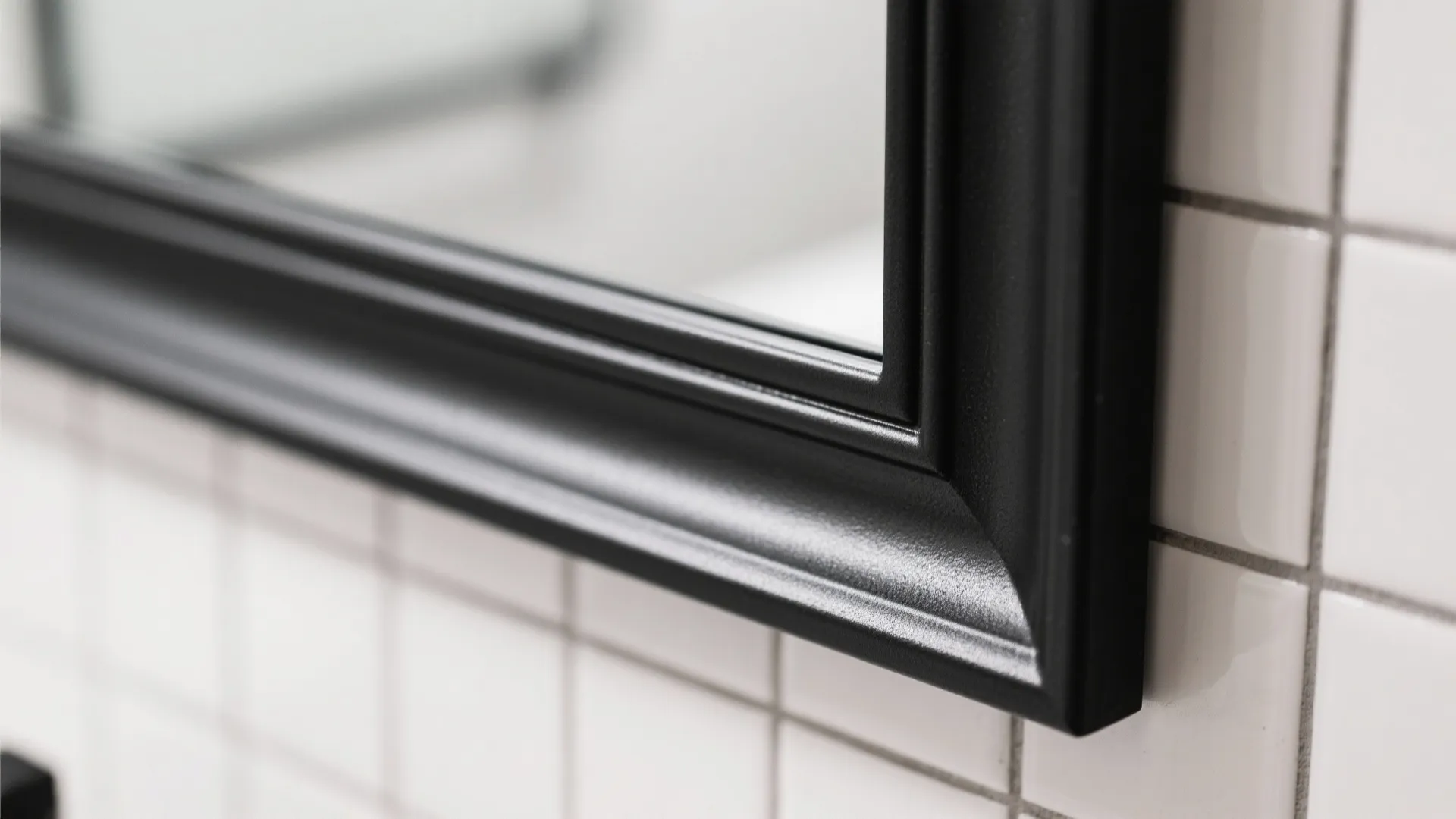 Close-up of a black metal mirror frame with a crisp mitered corner on light tile.