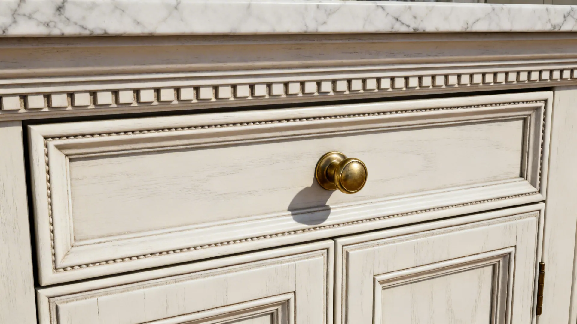 Macro detail of classical framed cabinet bead, brass hardware, and crown molding with marble counter edge.
