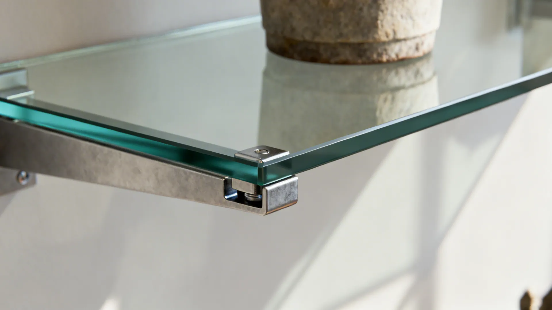 Macro view of a frameless glass shelf secured with concealed clips and a single display object.
