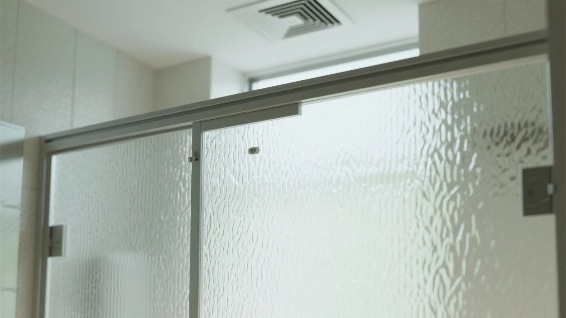 Close up view of frosted glass shower screen and a ceiling vent in white bathroom
