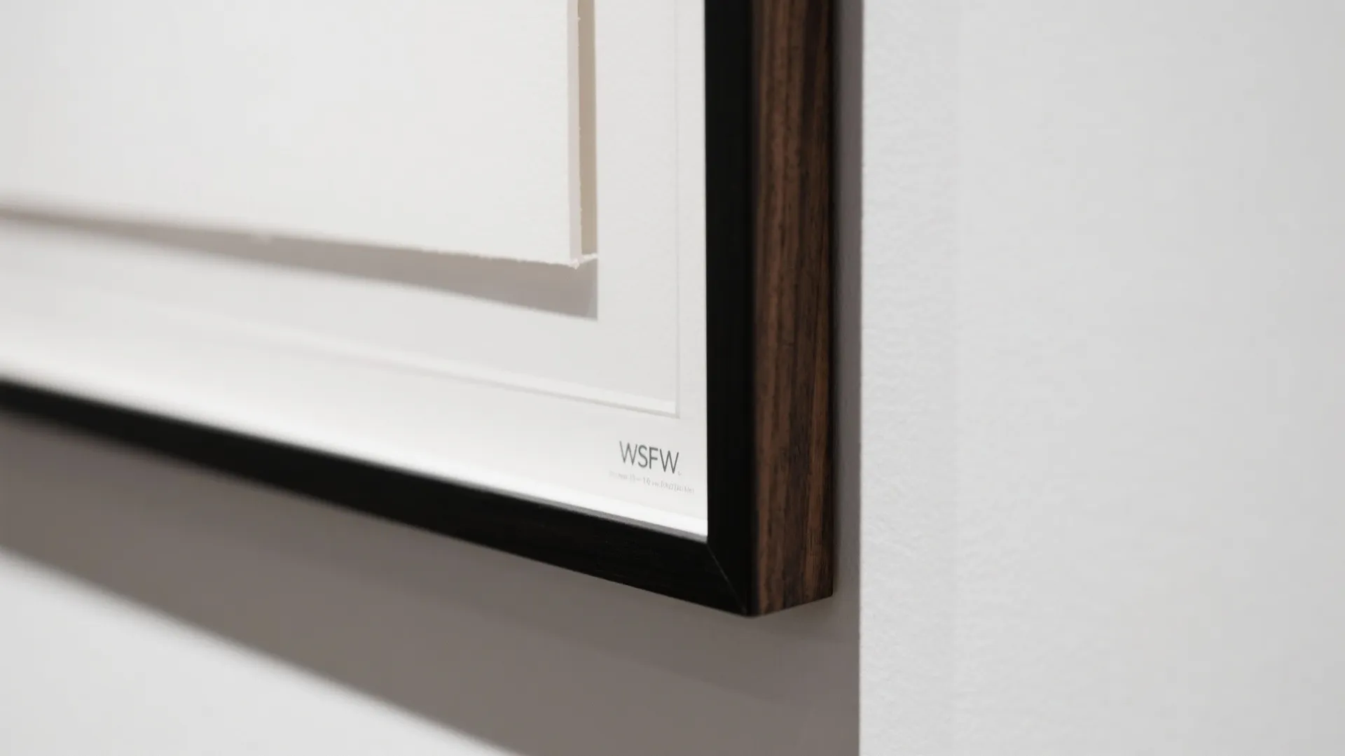 Close up view of a dark wooden picture frame hanging on a white gallery wall