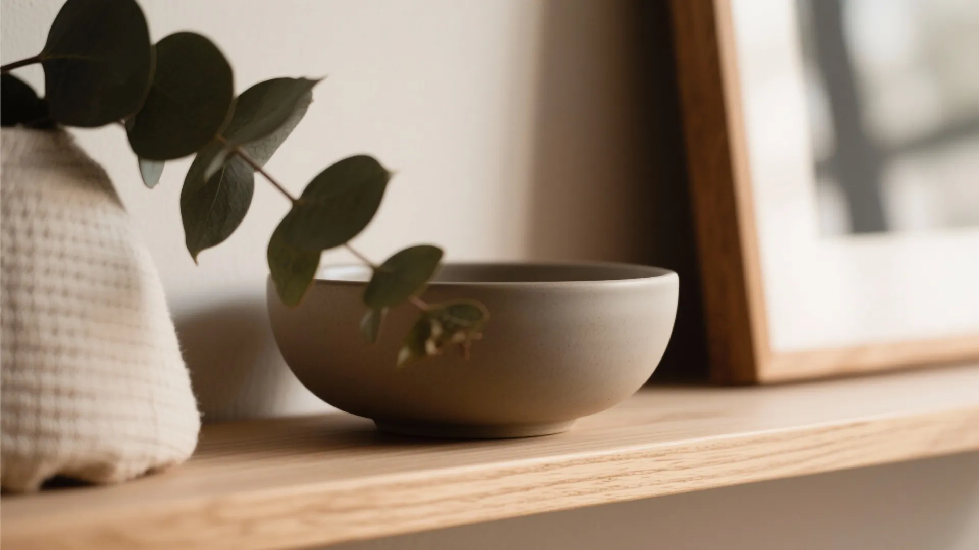 Macro of oak shelf vignette with matte ceramic bowl, linen, and plant leaves.