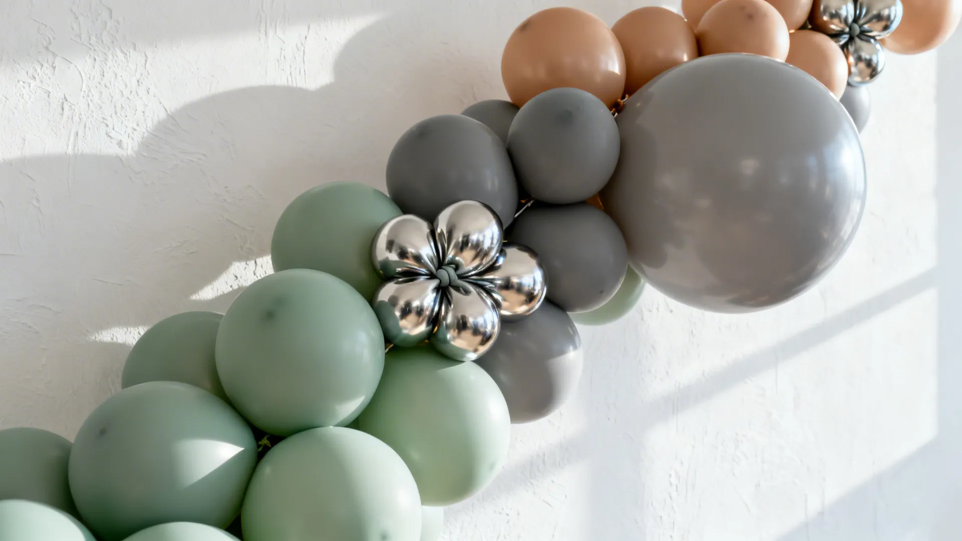 Green grey and peach balloons with silver flower balloon decoration against a textured white wall