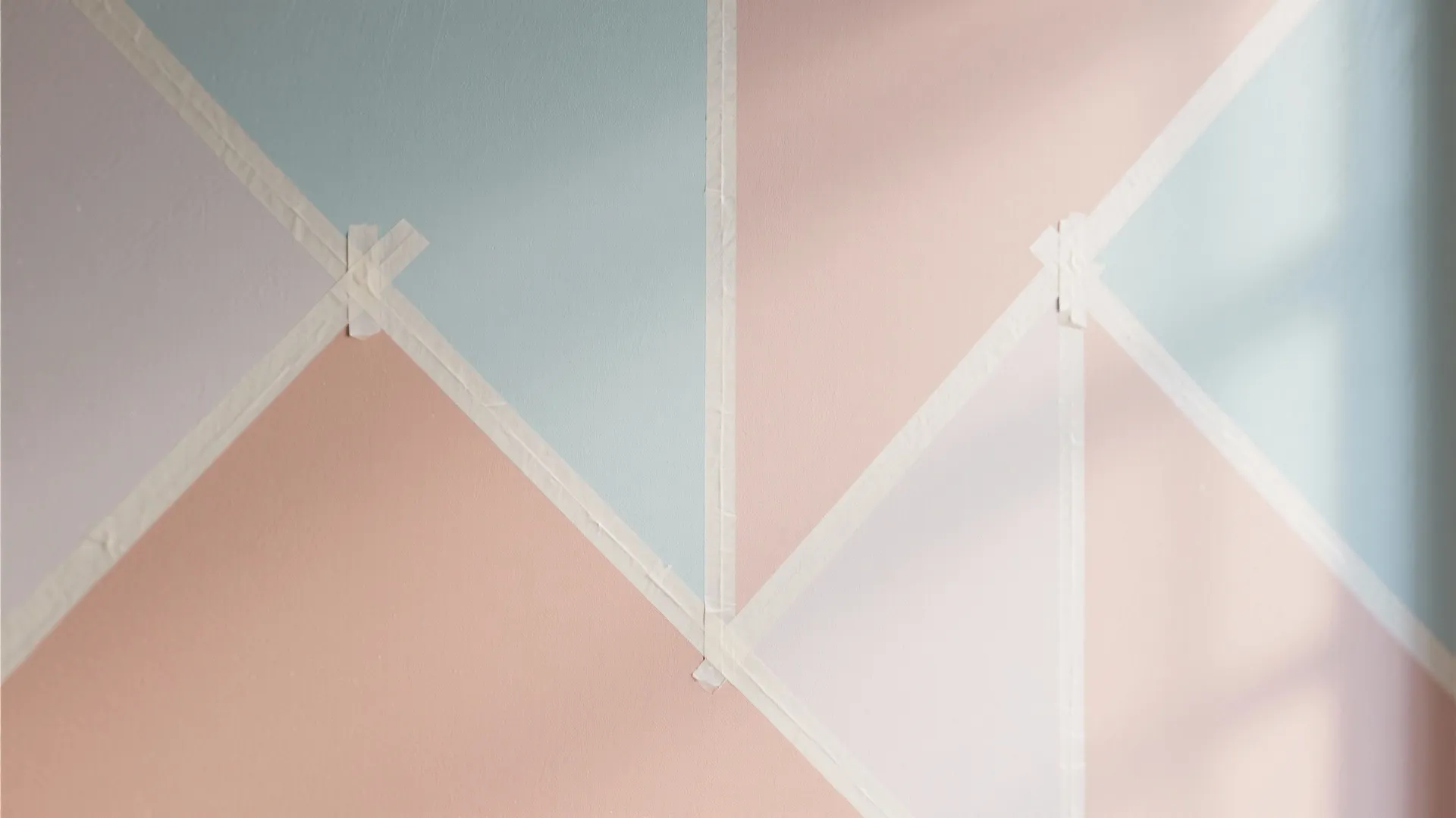Wall painting project using masking tape to create geometric patterns in pastel pink and blue