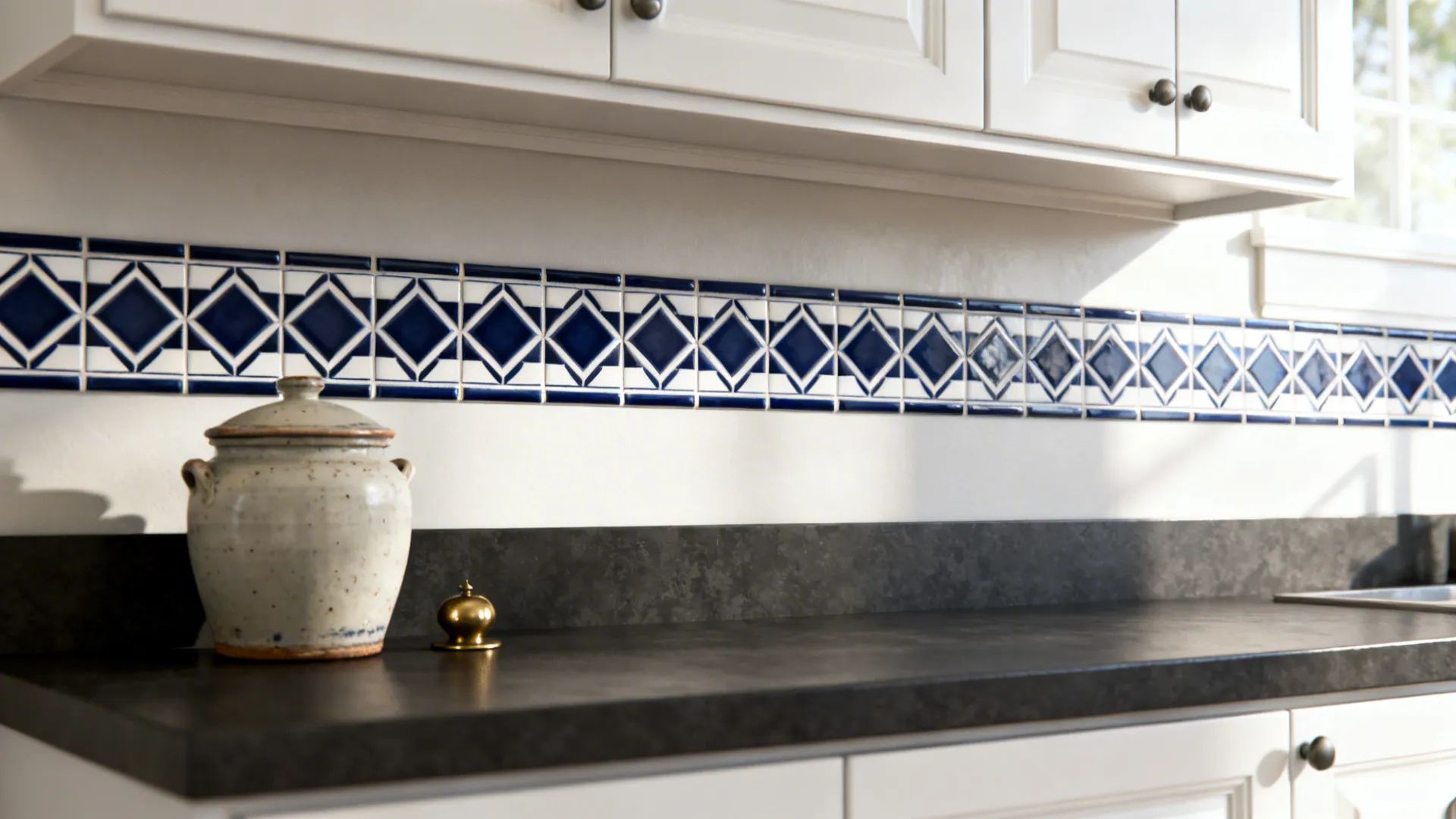 Navy and white geometric tile accent strip above dark countertop and white cabinets