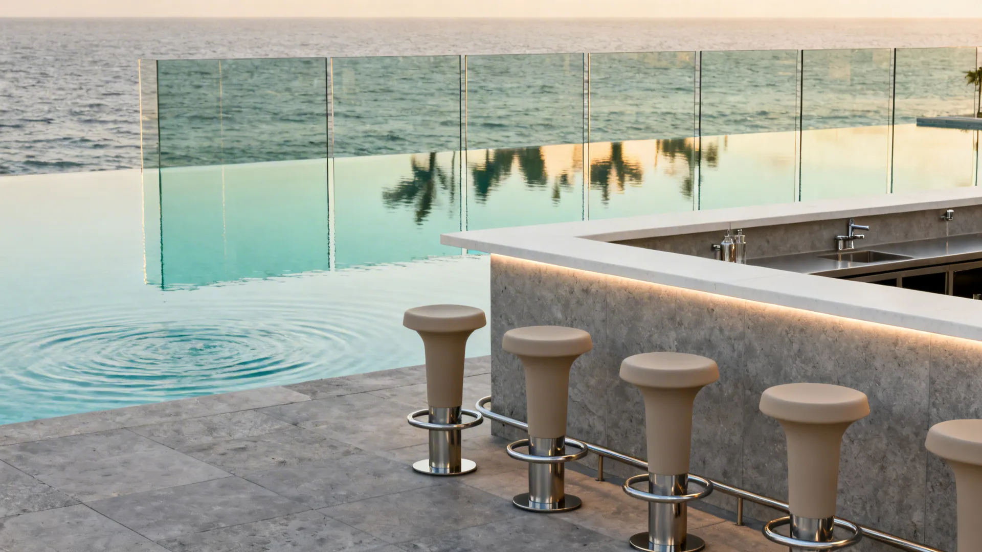 Outdoor stone bar with beige chairs next to a swimming pool overlooking the blue ocean