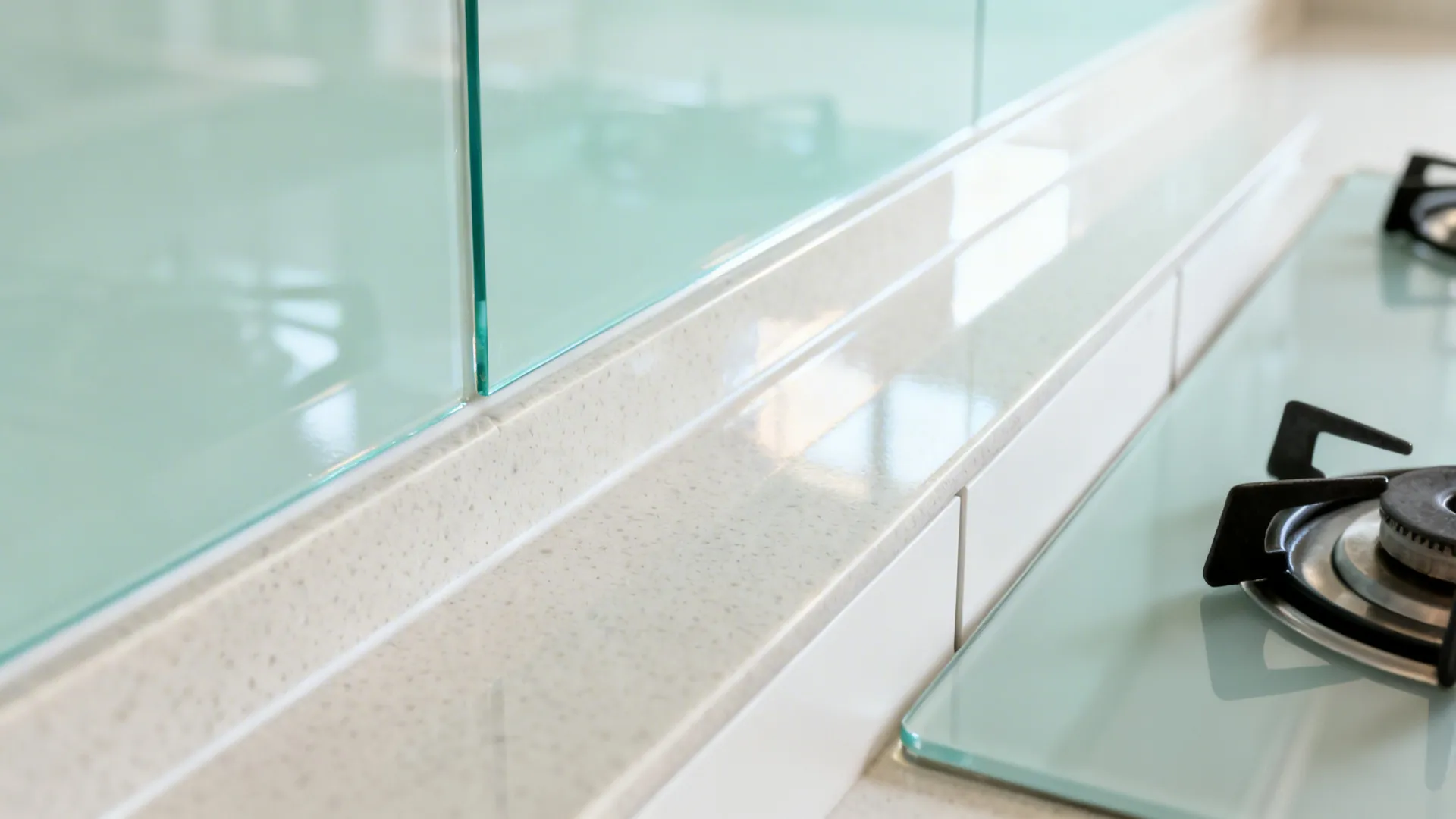 Close-up of a pale mint low-iron tempered glass backsplash meeting a light quartz countertop.