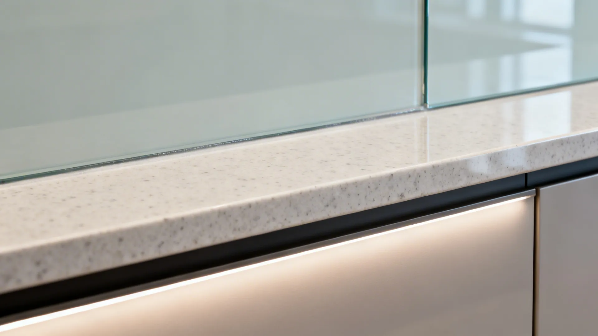 Close-up of back-painted glass backsplash with quartz counter and even task lighting.