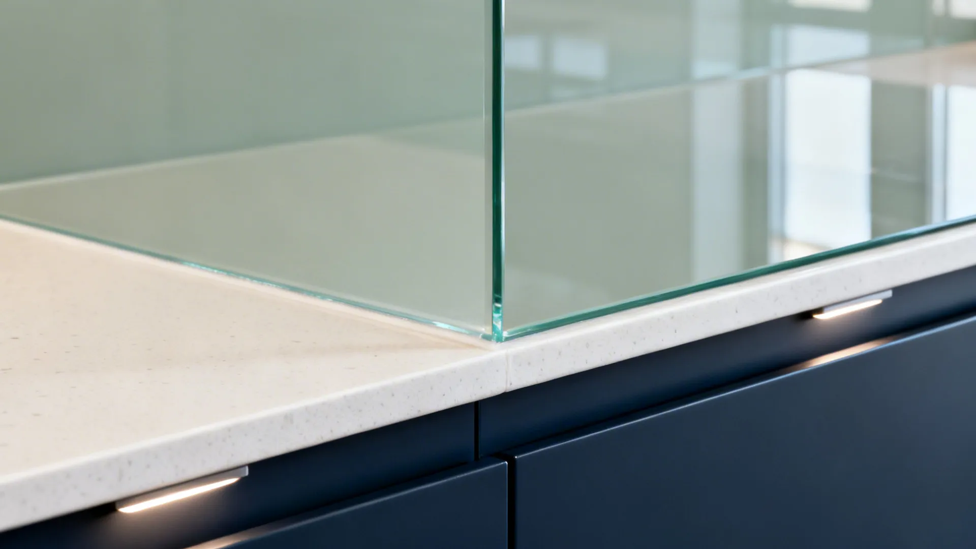 Close-up of low-iron glass backsplash with off-white quartz counter and navy cabinetry.