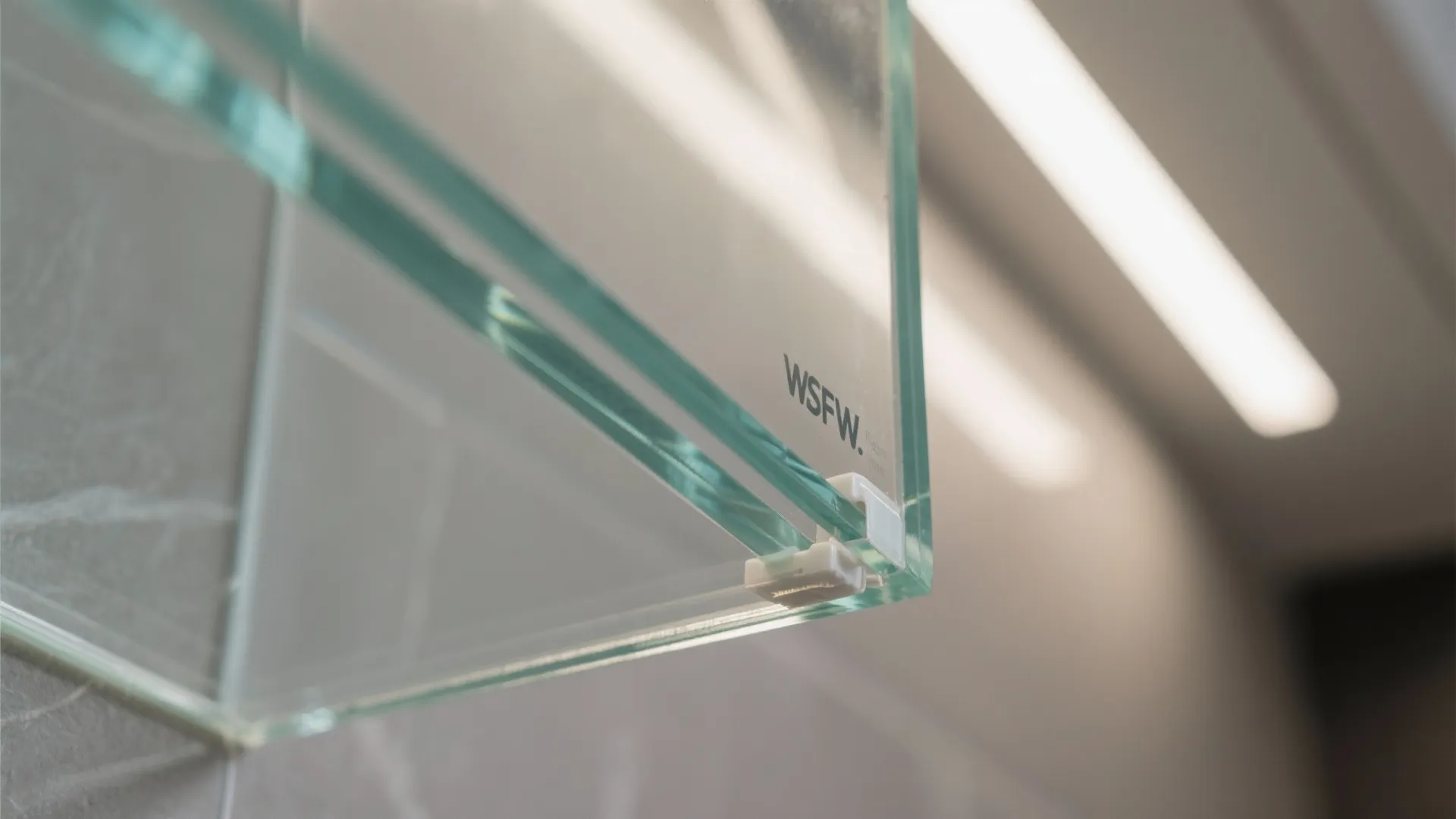 Close up of clear glass panel with white clip and logo on grey stone wall
