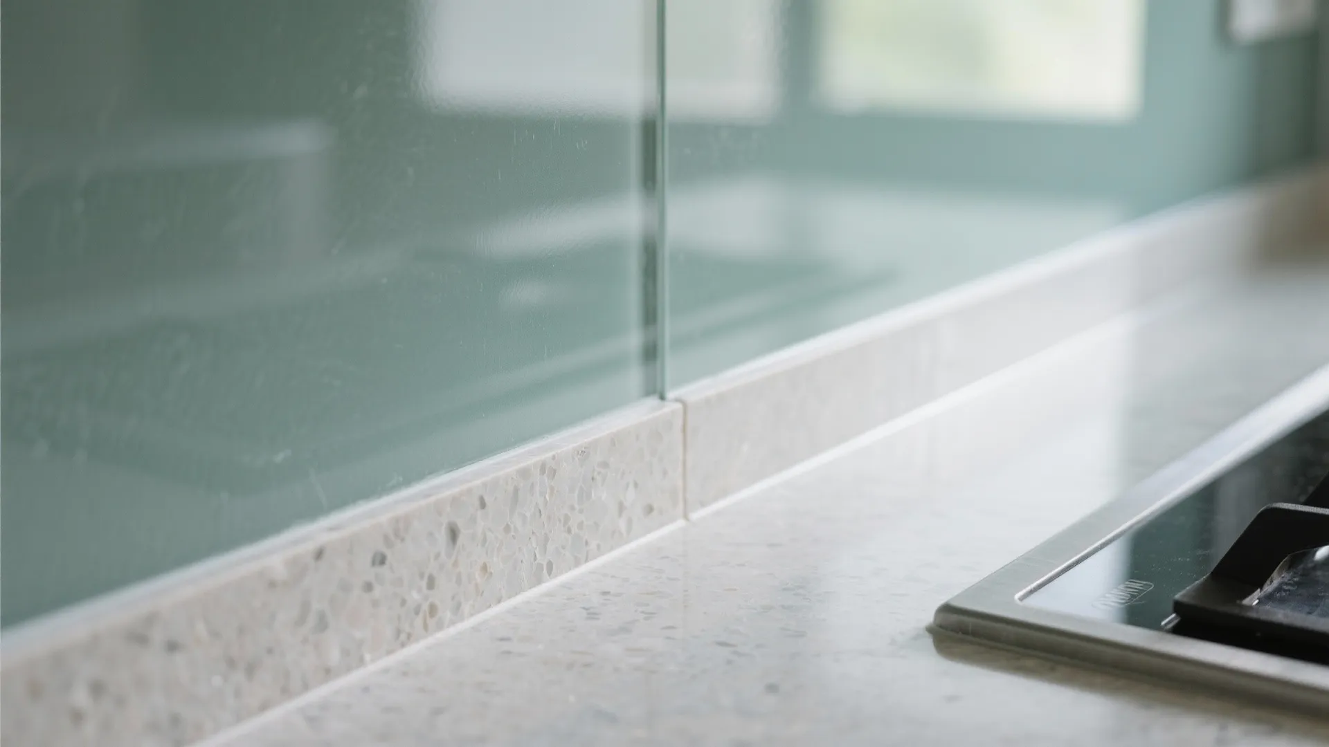 Close up view of light green glass wall panel and stone countertop in modern kitchen