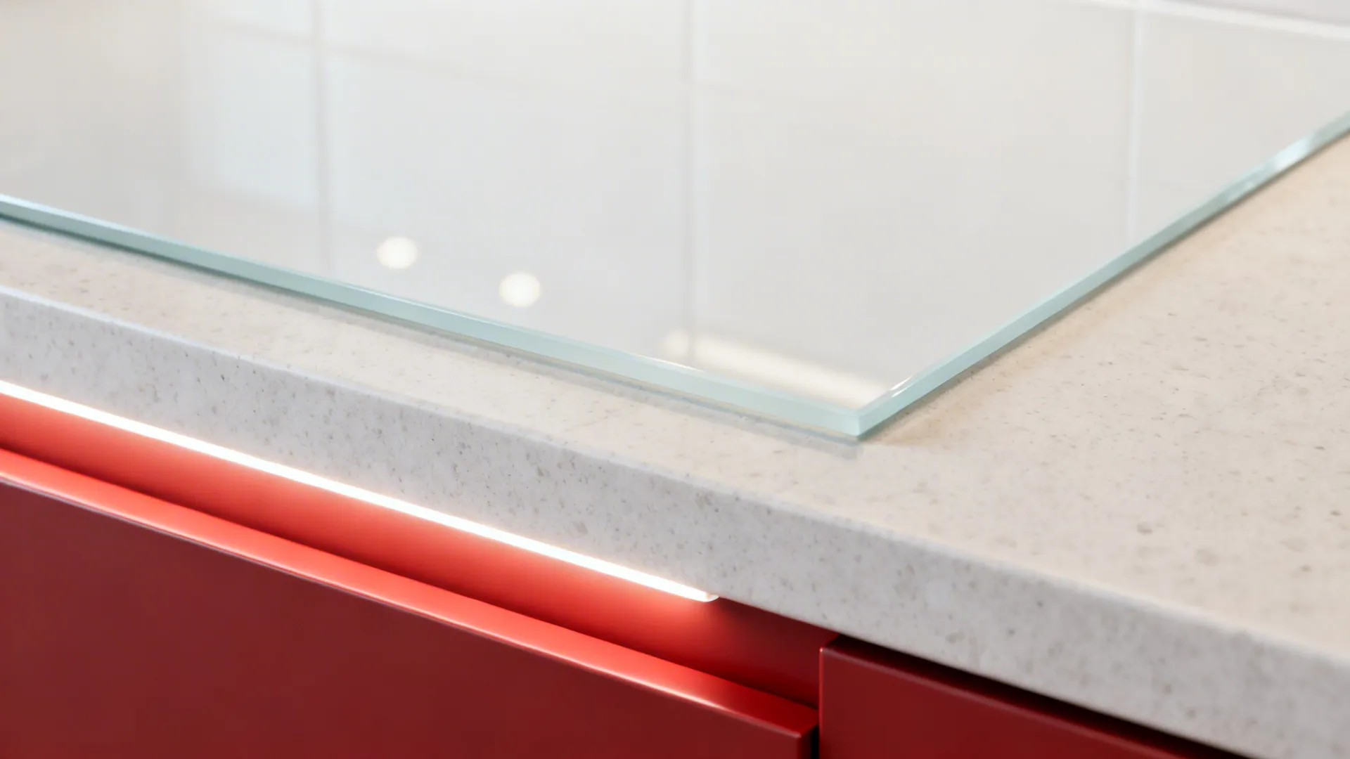 Close-up of white glass backsplash edge, quartz counter, and matte red drawer front
