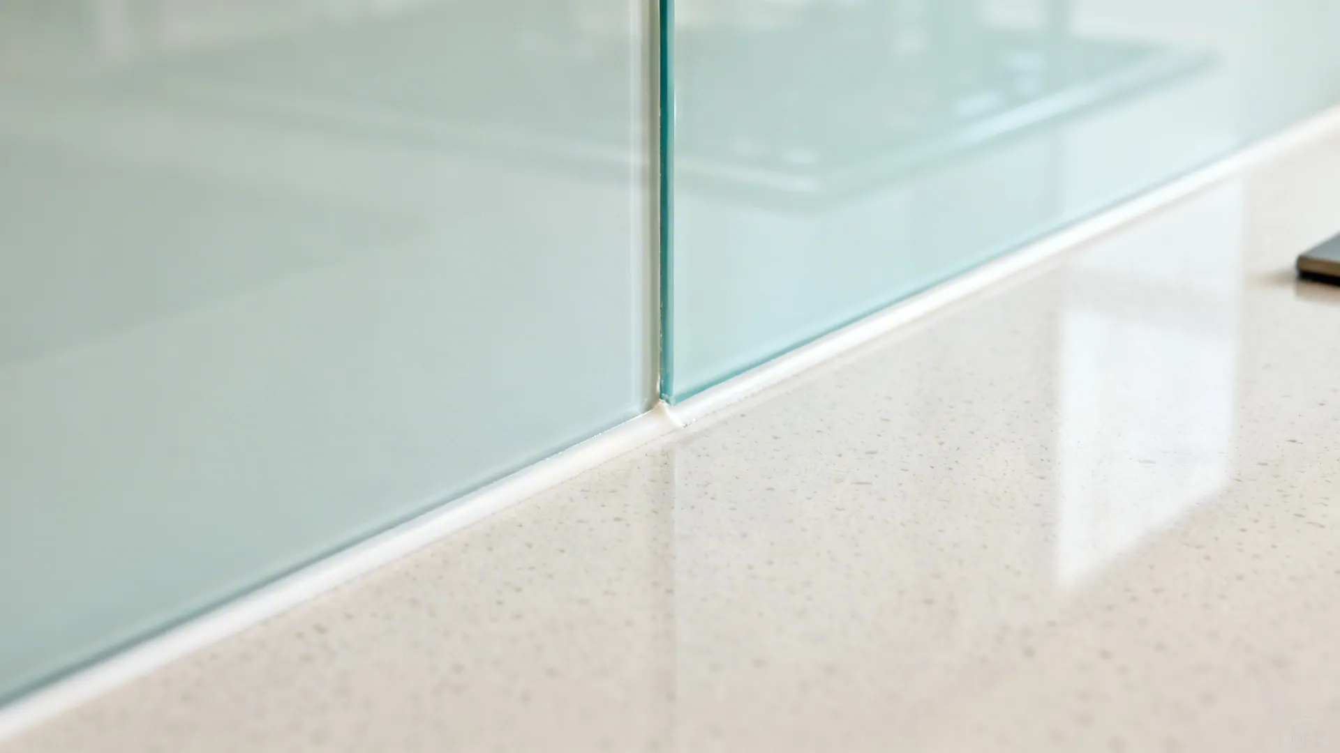 Close up of light blue glass wall panel meeting a white speckled stone kitchen counter top
