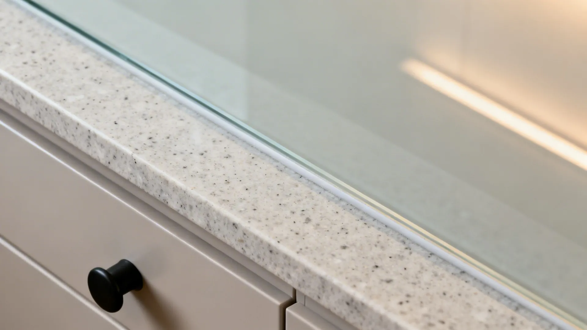 Macro of low-iron glass backsplash edge meeting quartz countertop under warm lighting.