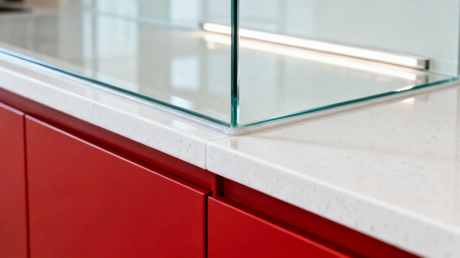 Macro detail of low-iron glass backsplash with white quartz and red cabinet edge.