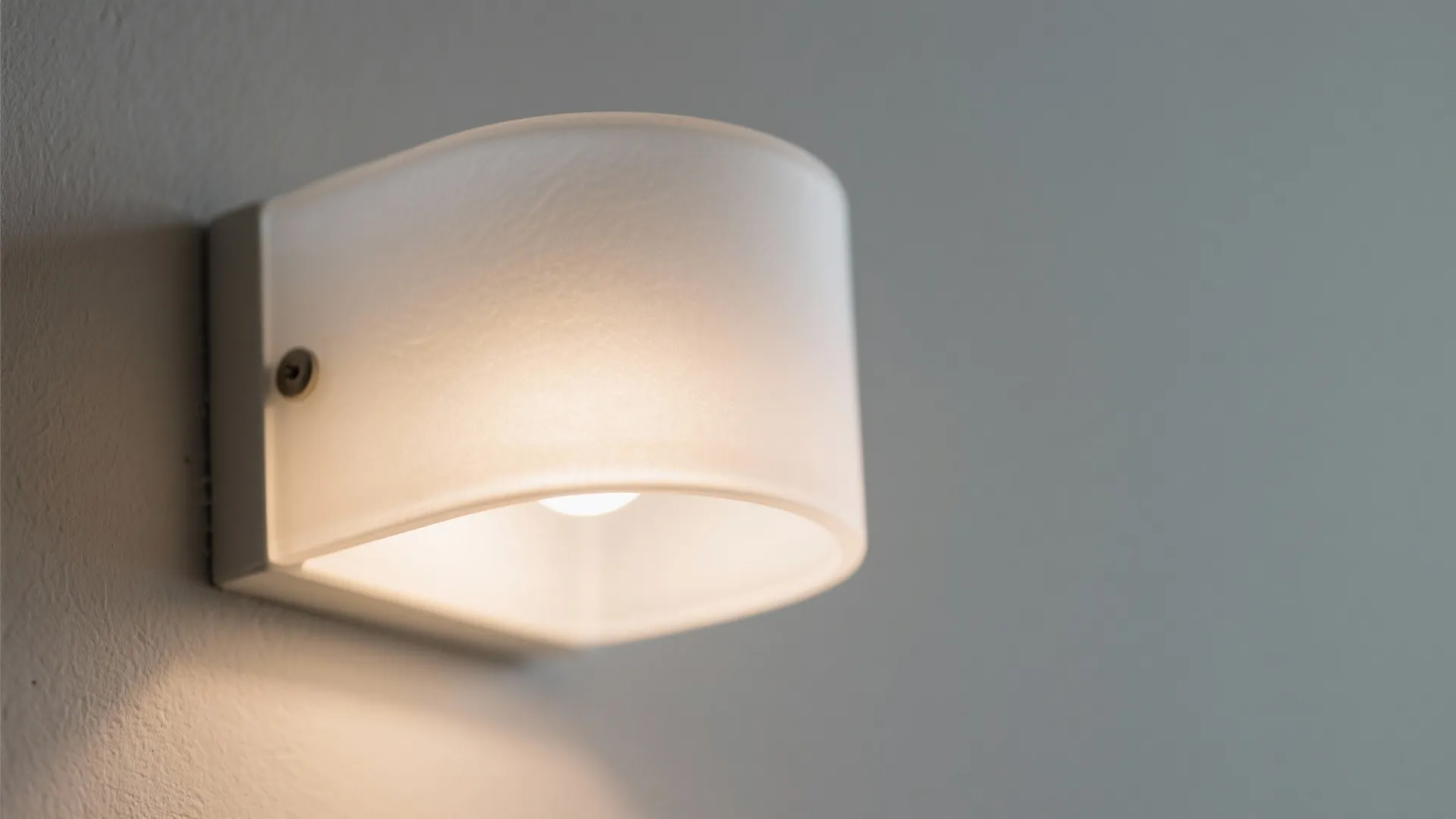 Close up of a simple white wall light fixture with a warm glowing light bulb