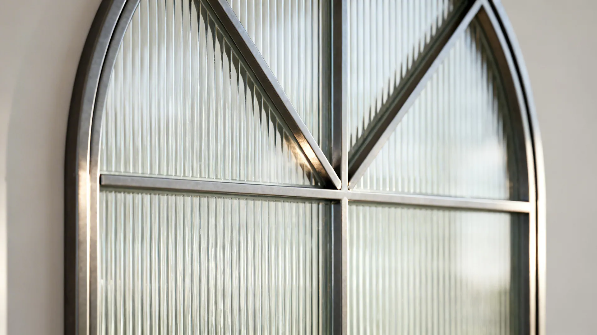Macro detail of slim steel frame and reeded glass at an arched door junction.